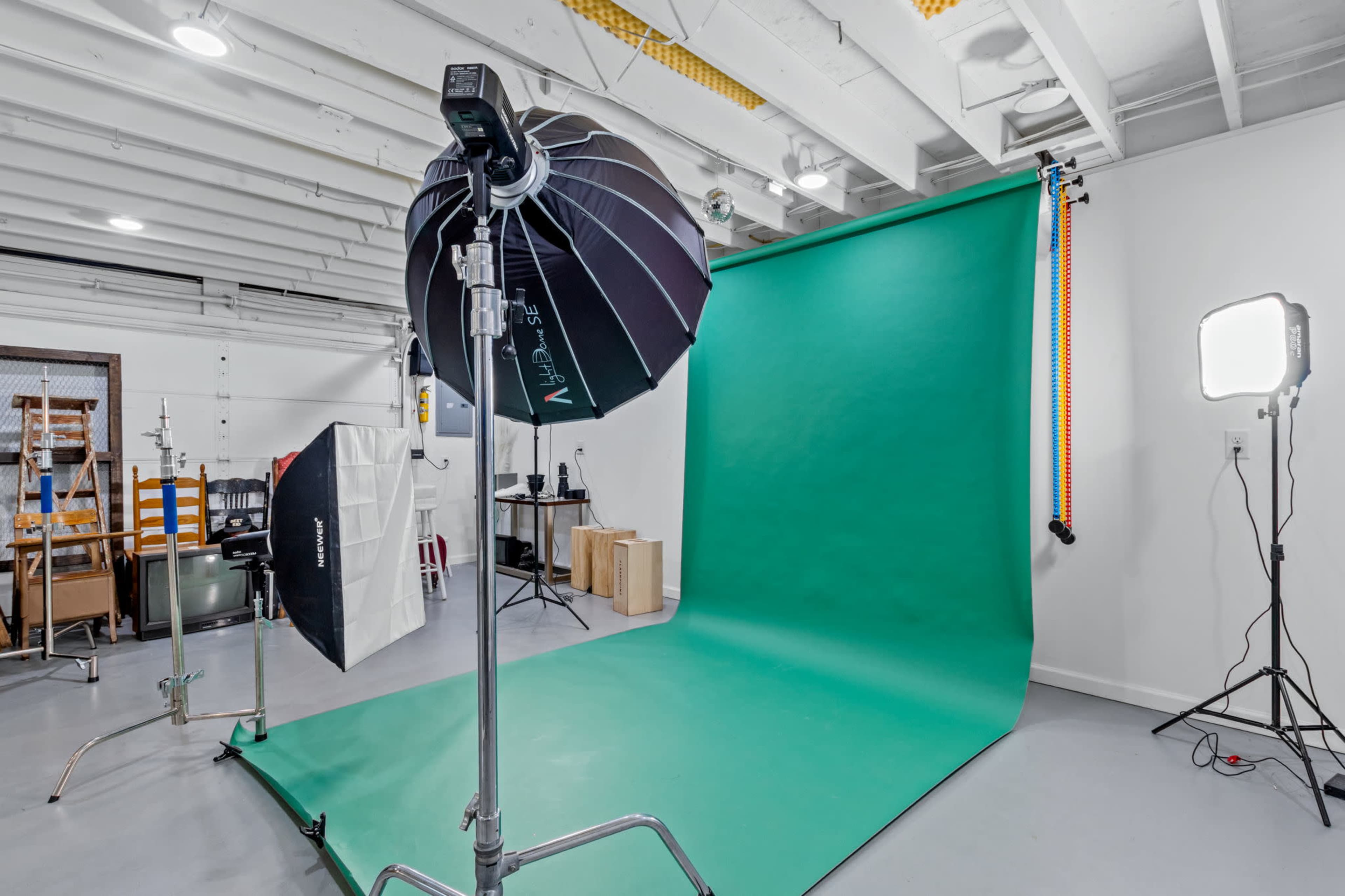 The image shows a photography studio with a green backdrop, lighting equipment, and various other photography tools arranged neatly.