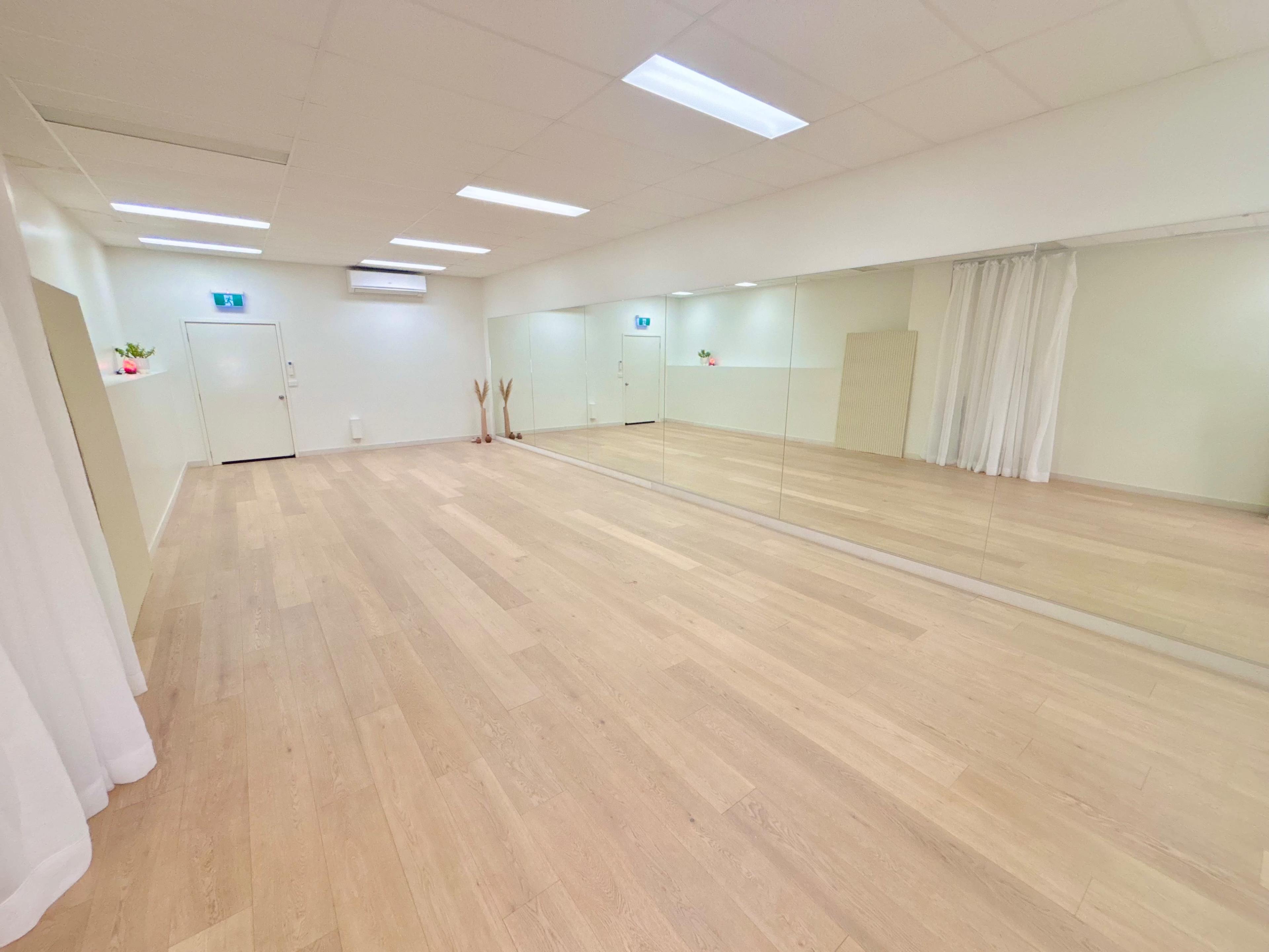The image shows a spacious, well-lit studio with wooden flooring and large mirrors along one wall.