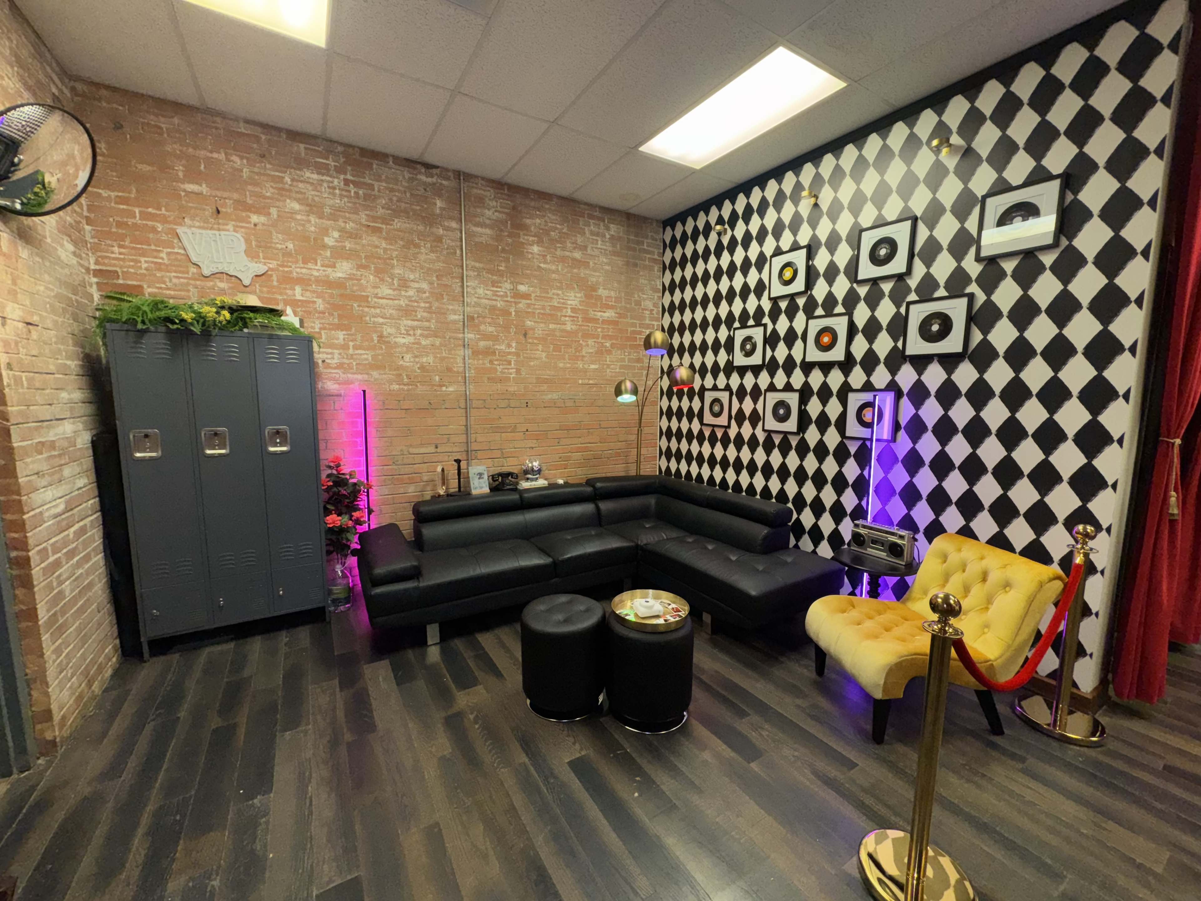 The image shows a modern lounge area with a black sectional couch, yellow tufted armchair, decorative black and white checkered wall, and black lockers.