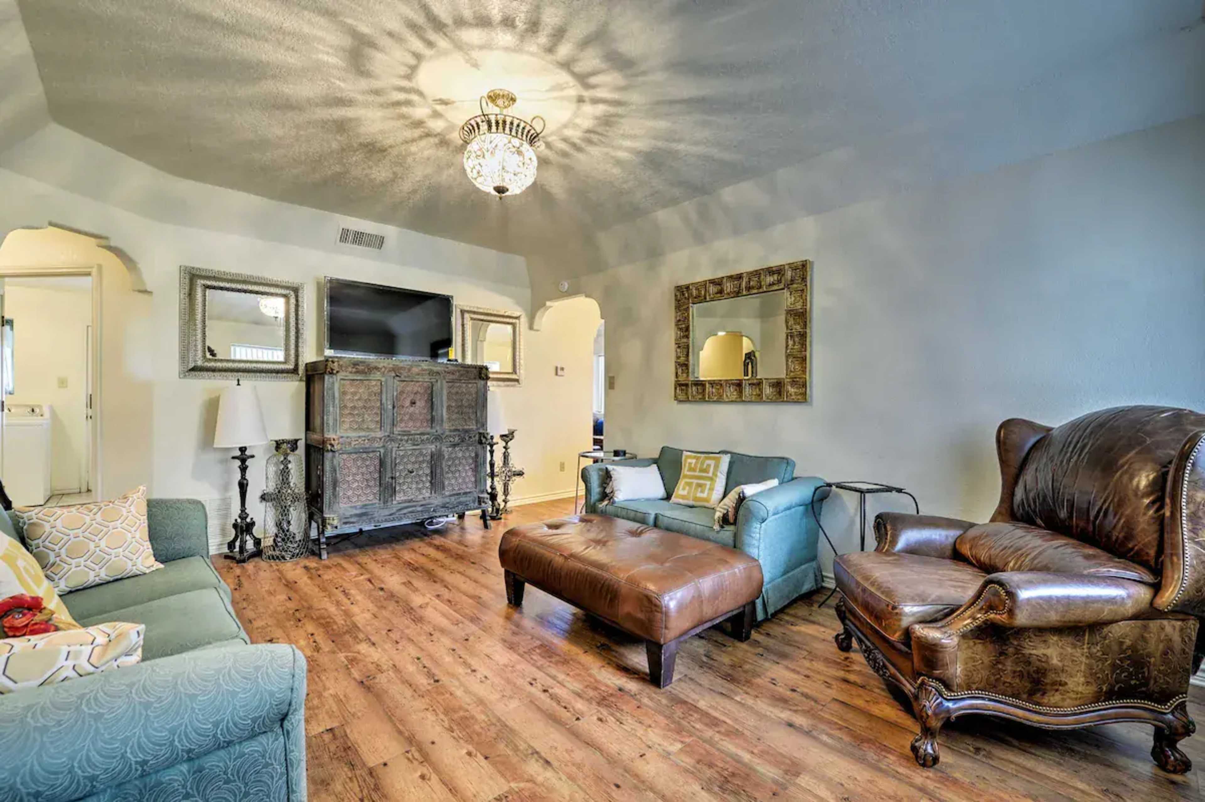 The living room features a chandelier above a couch, a large wooden cabinet, a television, a leather chair, and a coffee table on hardwood flooring.