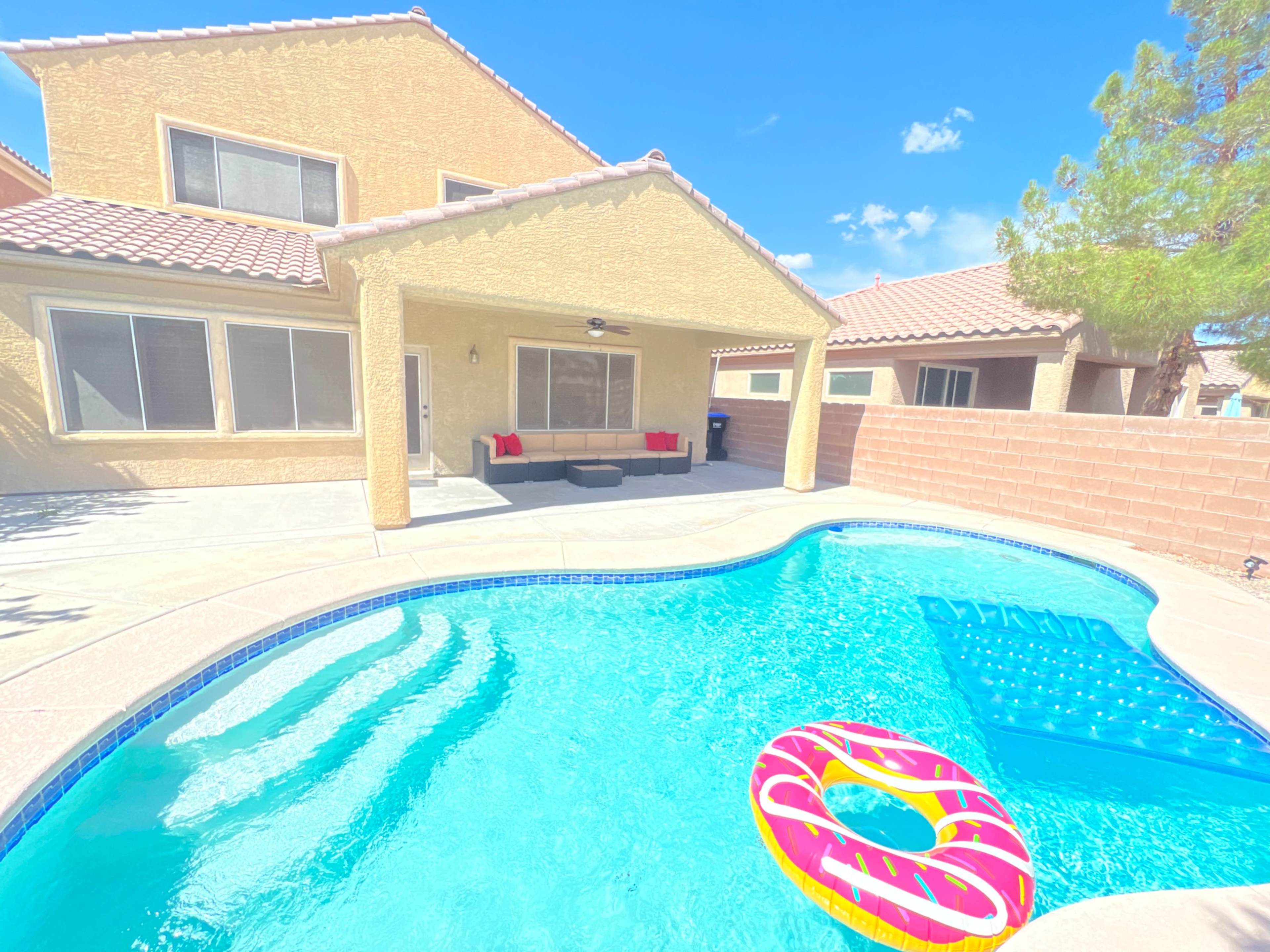 A backyard with a swimming pool, a lounge area with seating, and a colorful pool float.