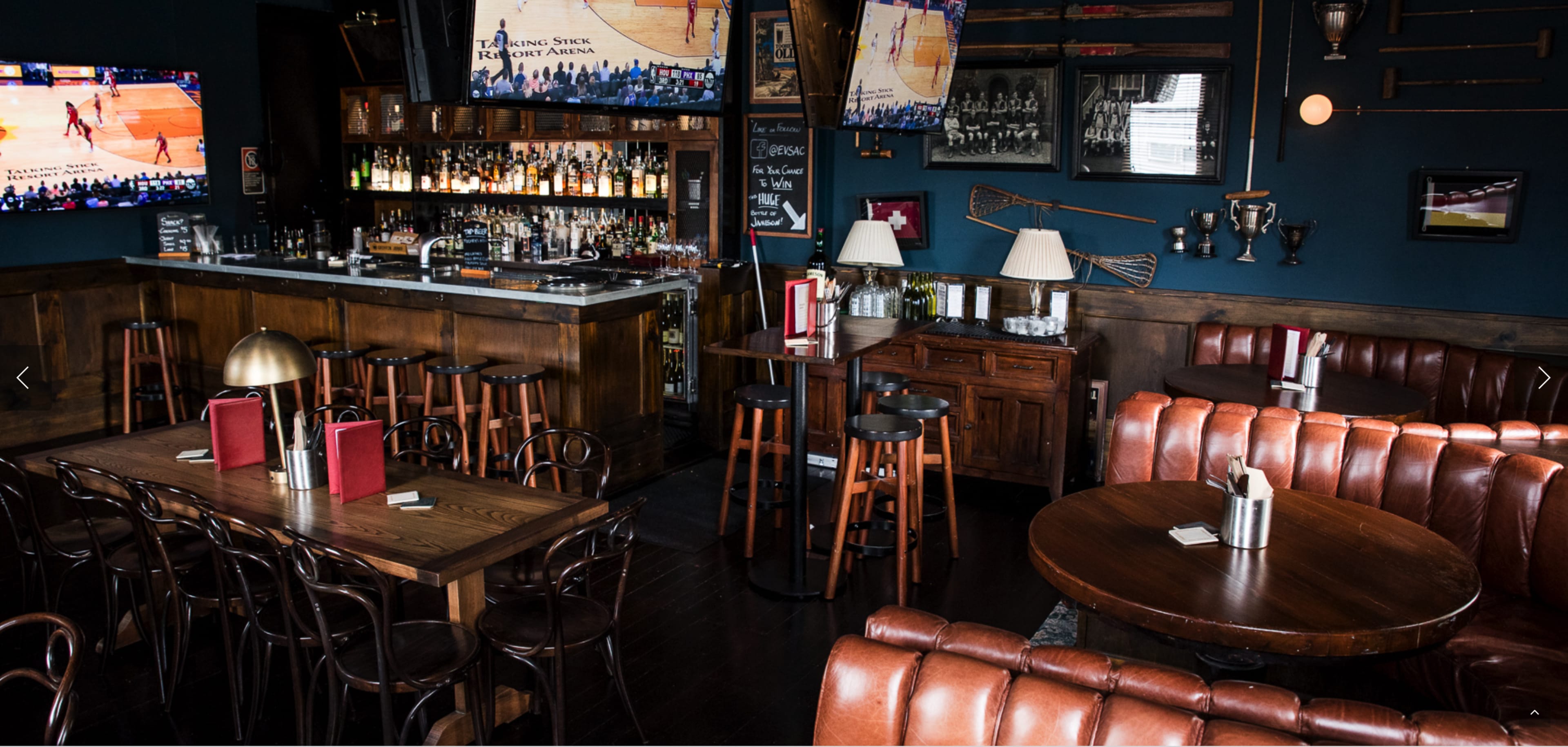A cozy sports bar with wooden furniture, multiple television screens displaying basketball games, and a well-stocked bar in the background.