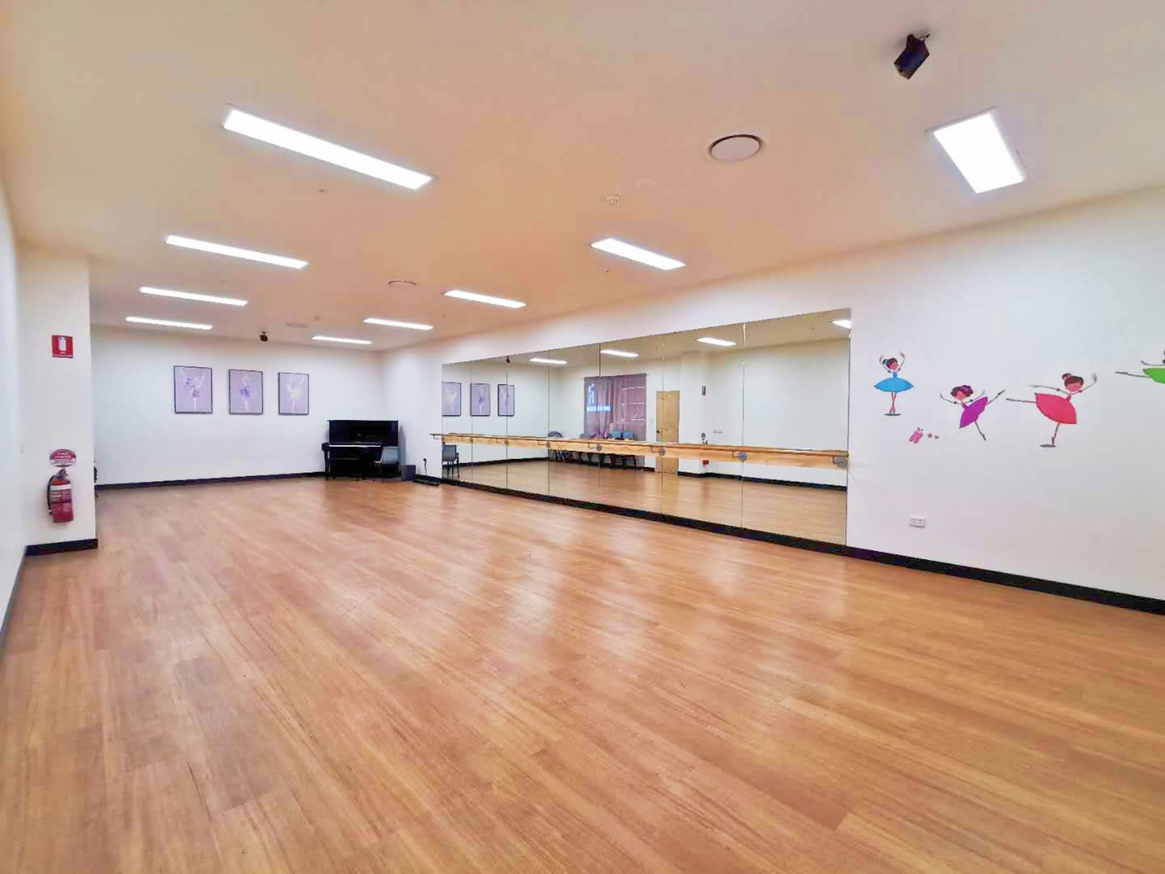 The image shows a spacious dance studio with wooden flooring, mirrors on one wall, and colorful ballet-themed decorations.