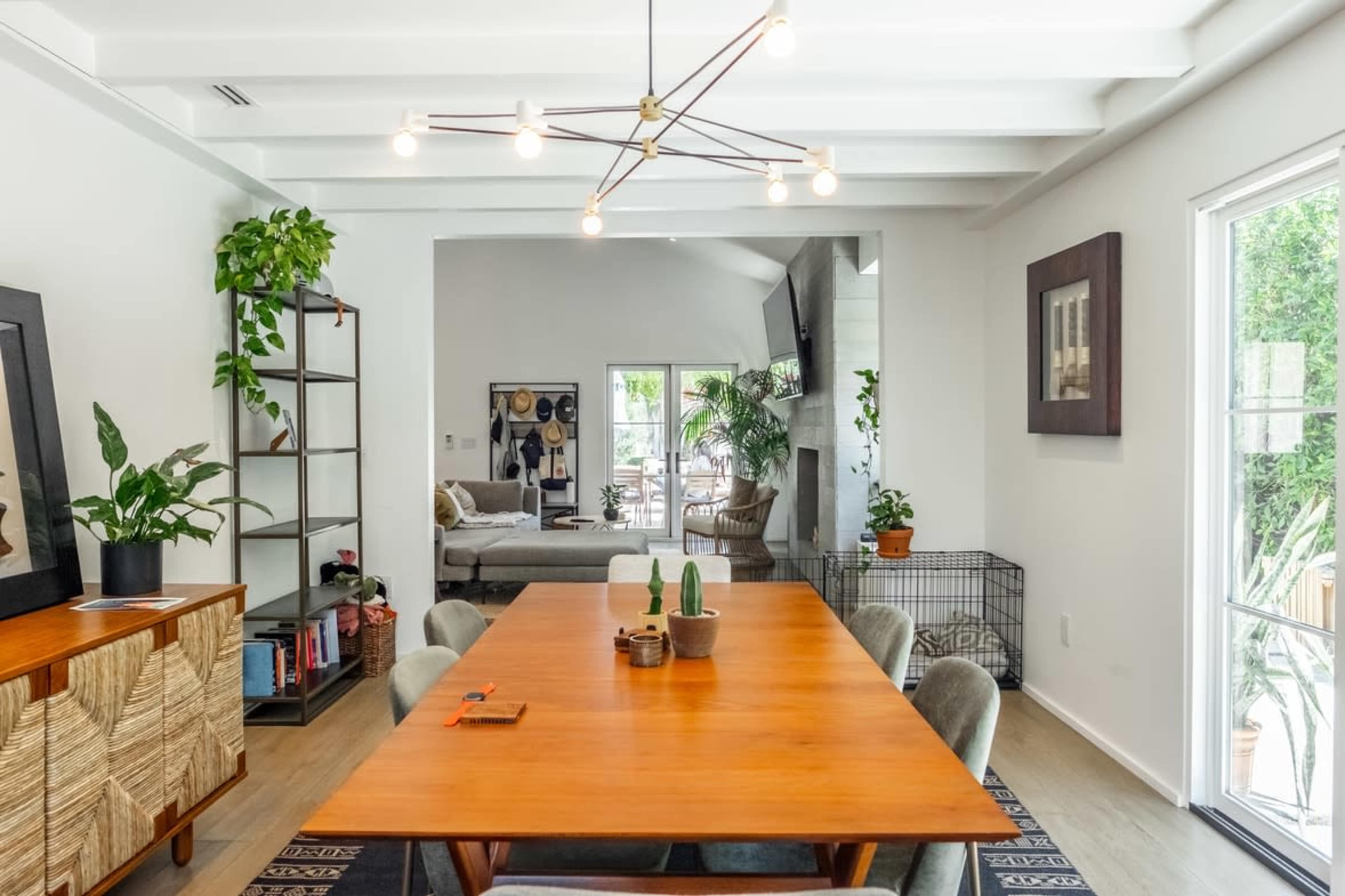 A dining area features a wooden table surrounded by upholstered chairs, with a bookshelf and a living space visible in the background.