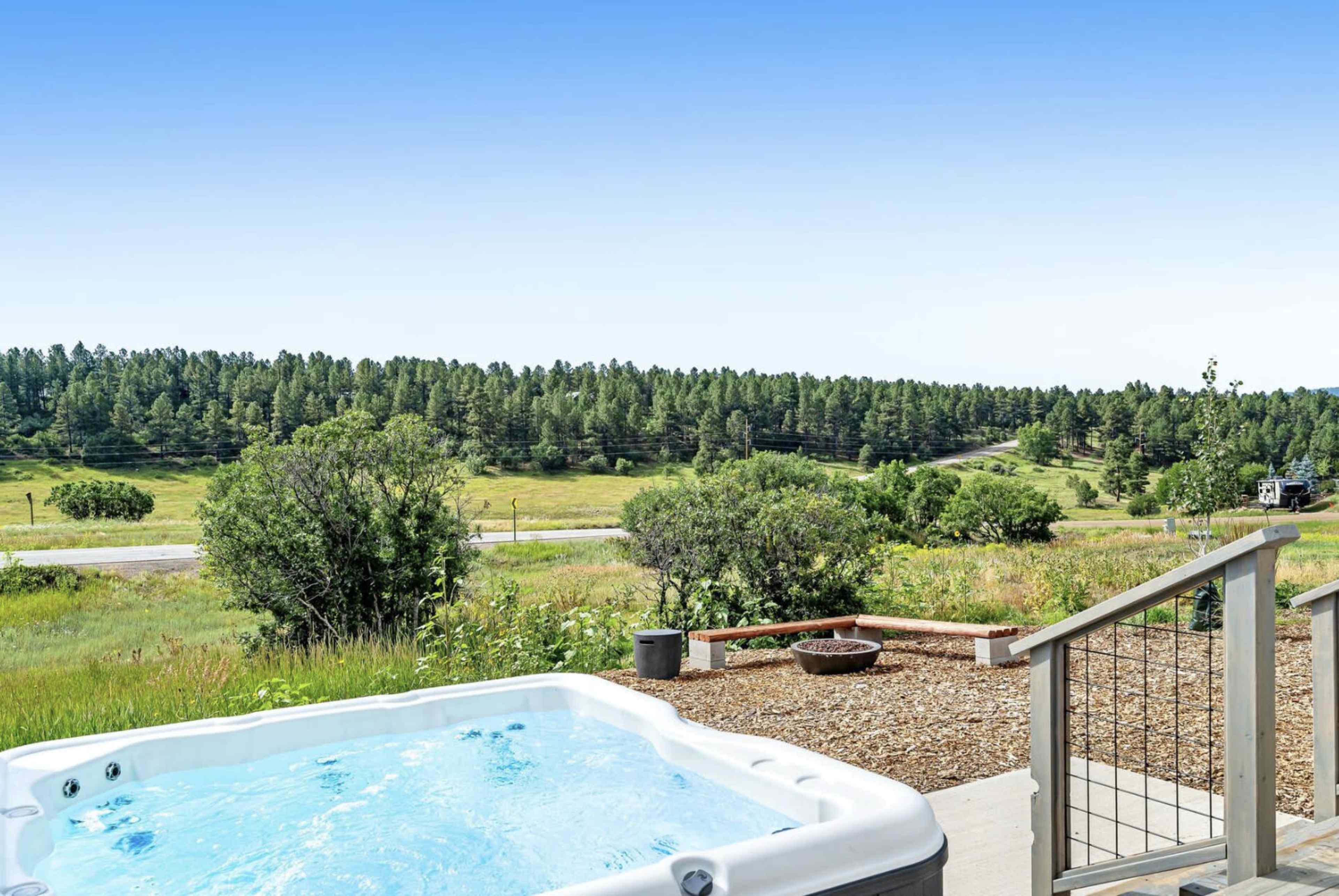 A hot tub is situated on a patio overlooking a green landscape with trees and a road in the background.