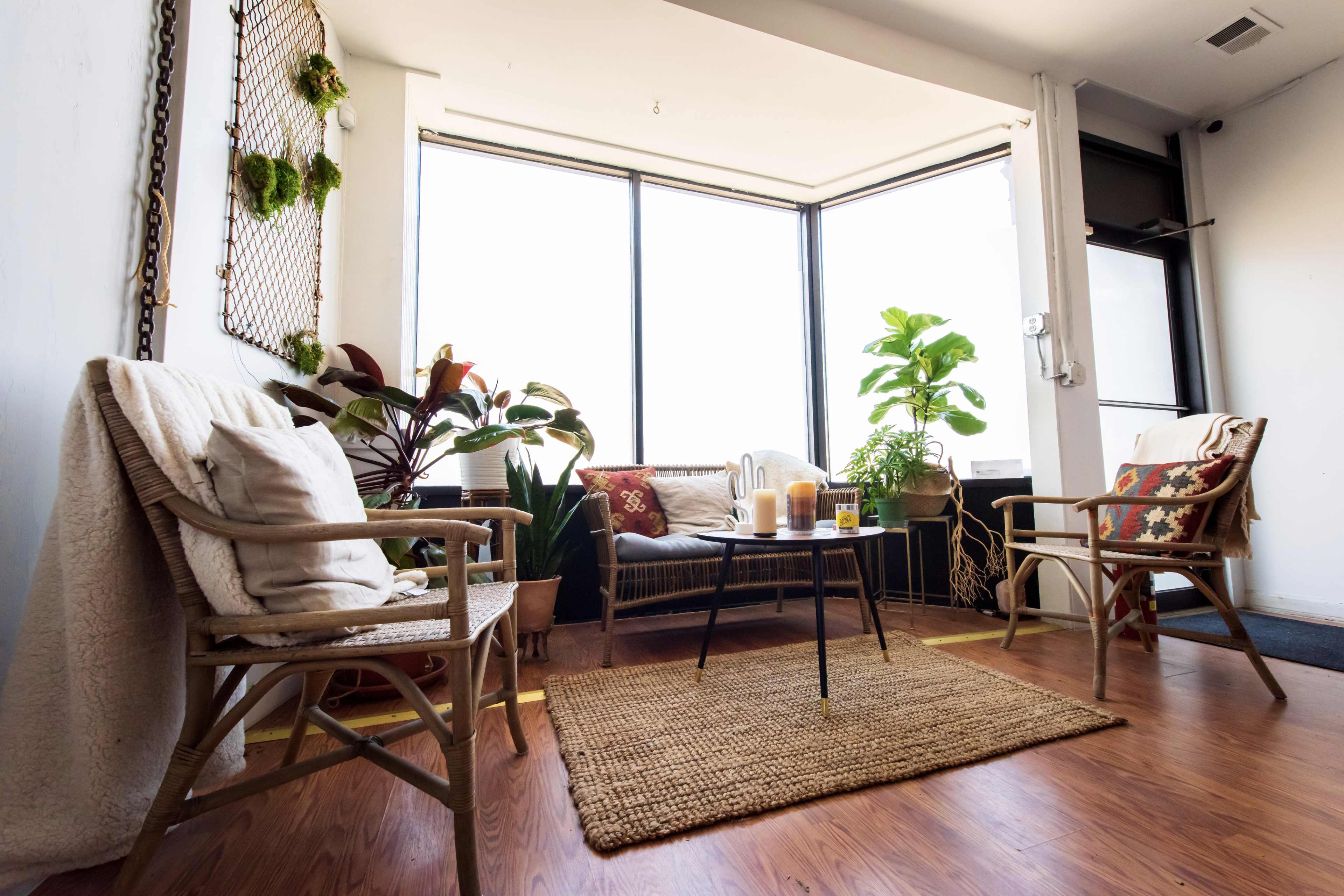 A cozy interior living space with a sofa, plants, and a coffee table surrounded by two chairs and a woven rug.