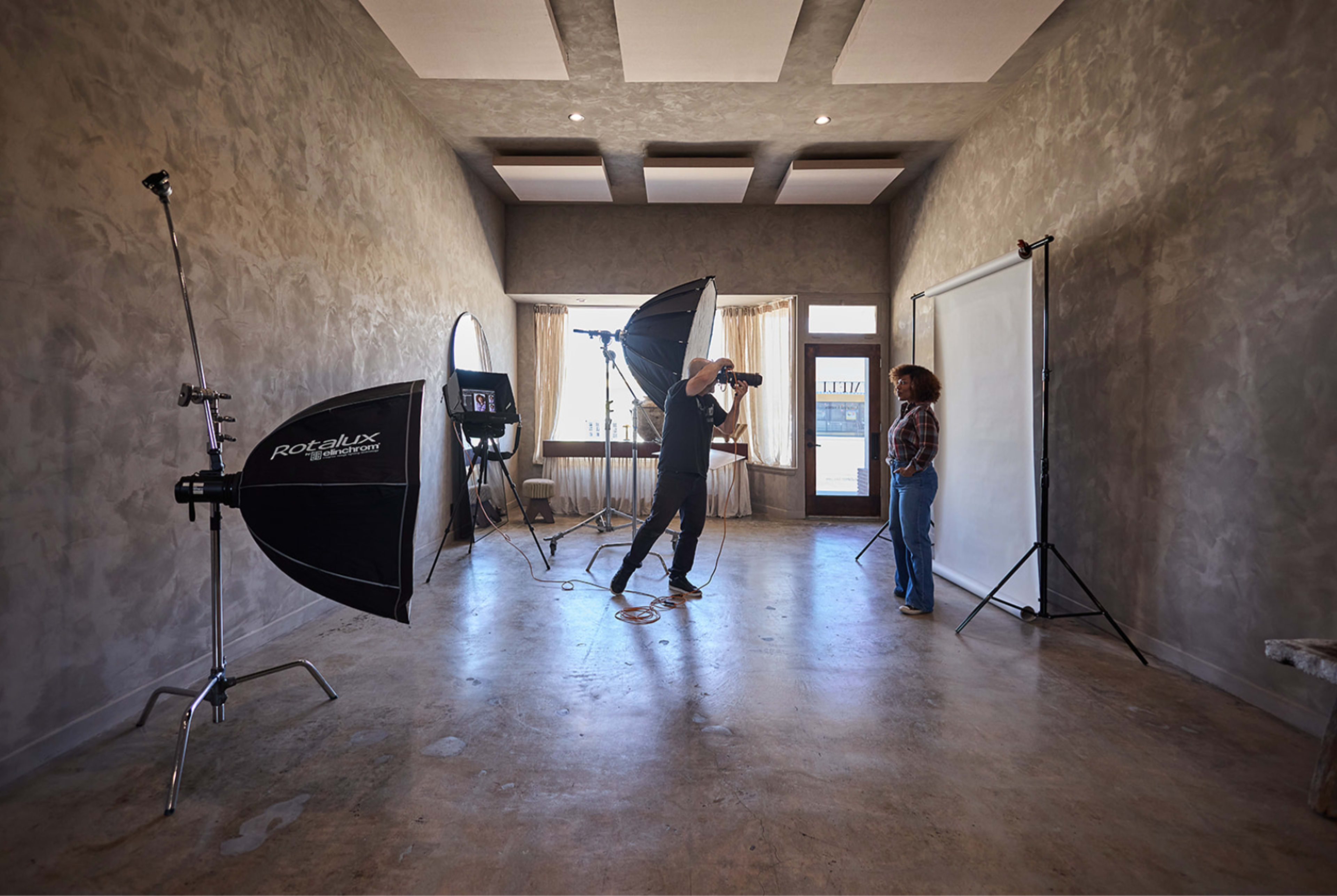 A photographer captures a subject in a minimalist studio space, equipped with softbox lights and a backdrop.