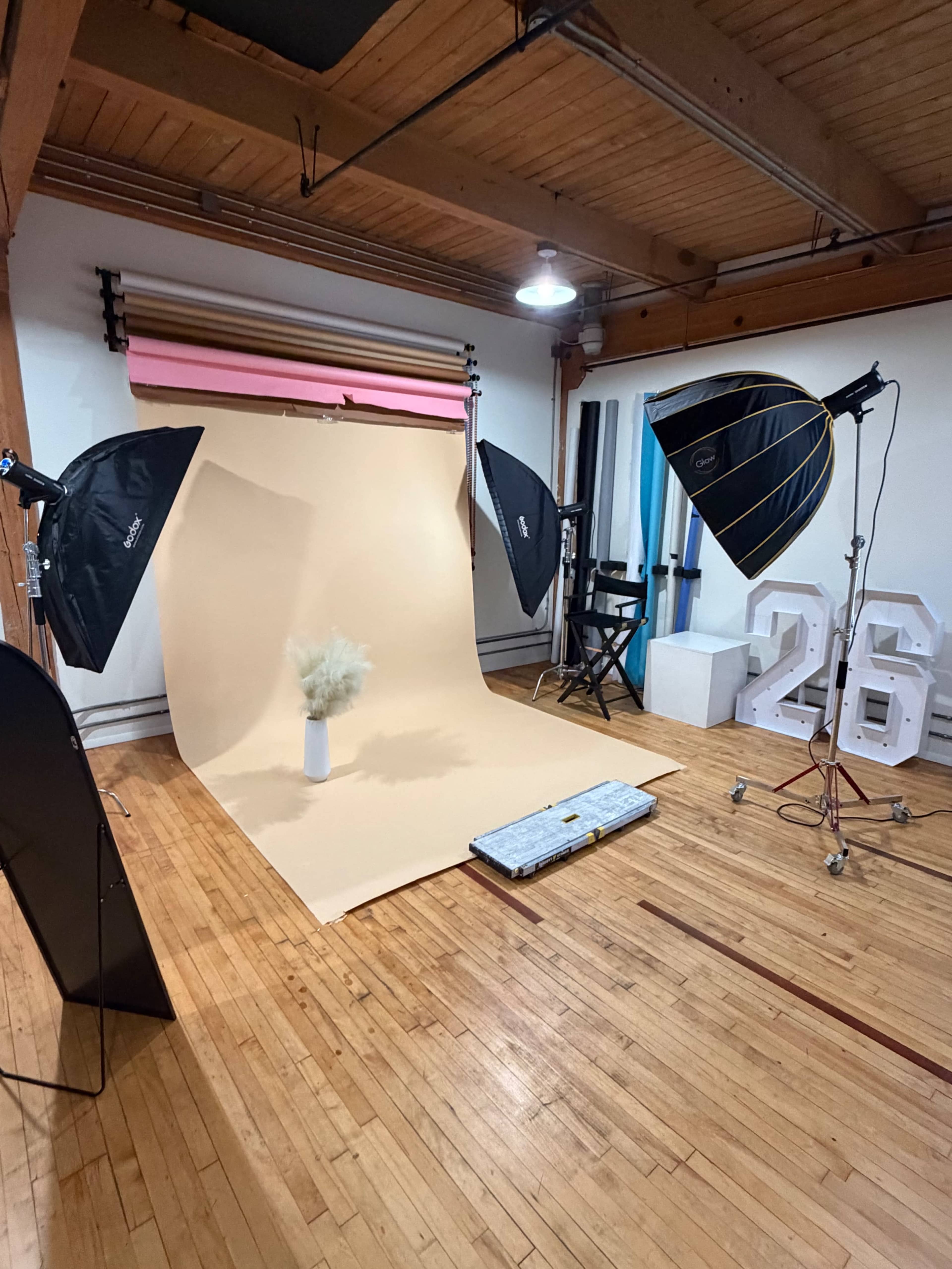 The image shows a photography studio with a seamless backdrop, lighting equipment, and a vase placed on the floor.