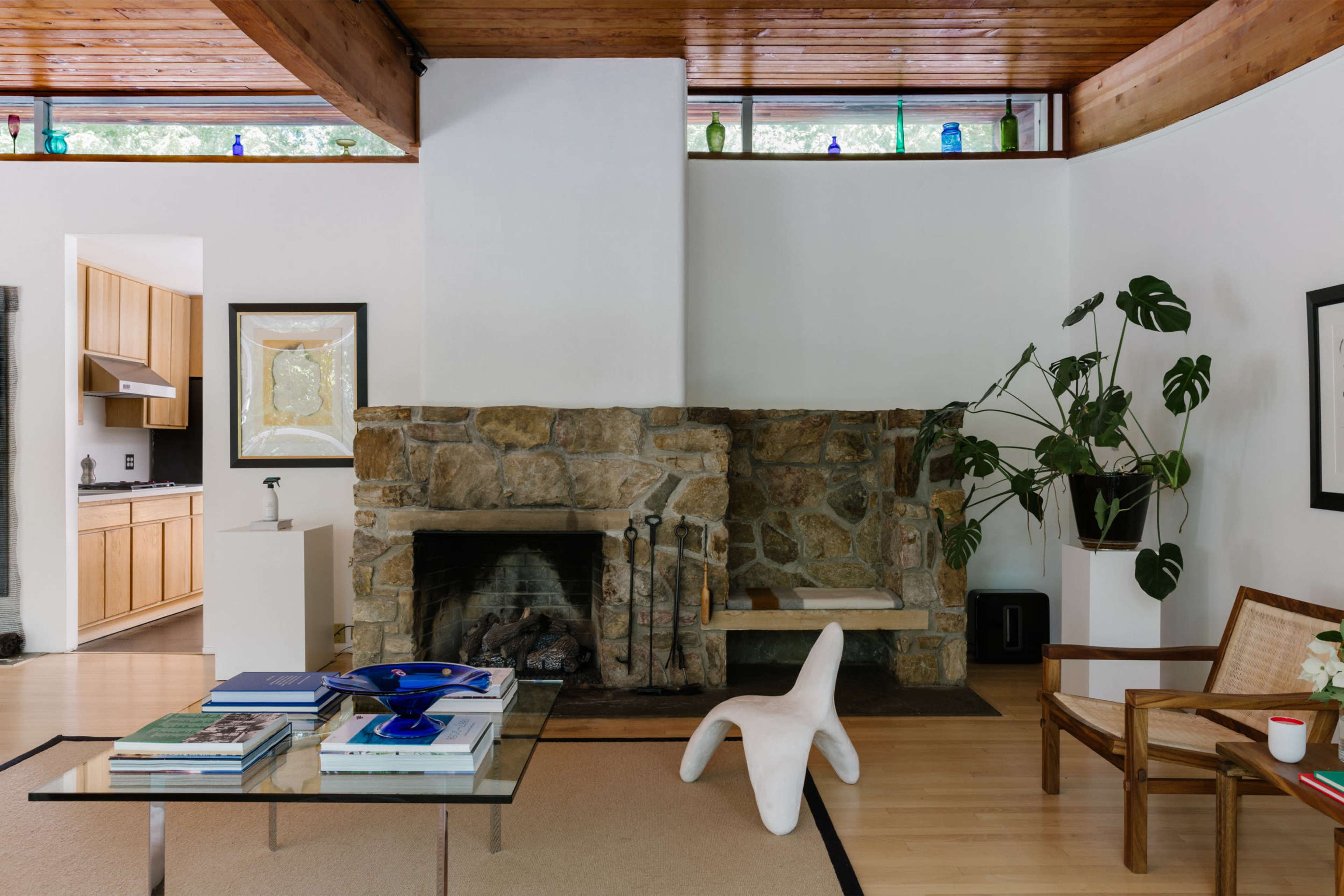 A modern living room featuring a stone fireplace, wooden beams on the ceiling, and a glass coffee table on a light-colored rug.