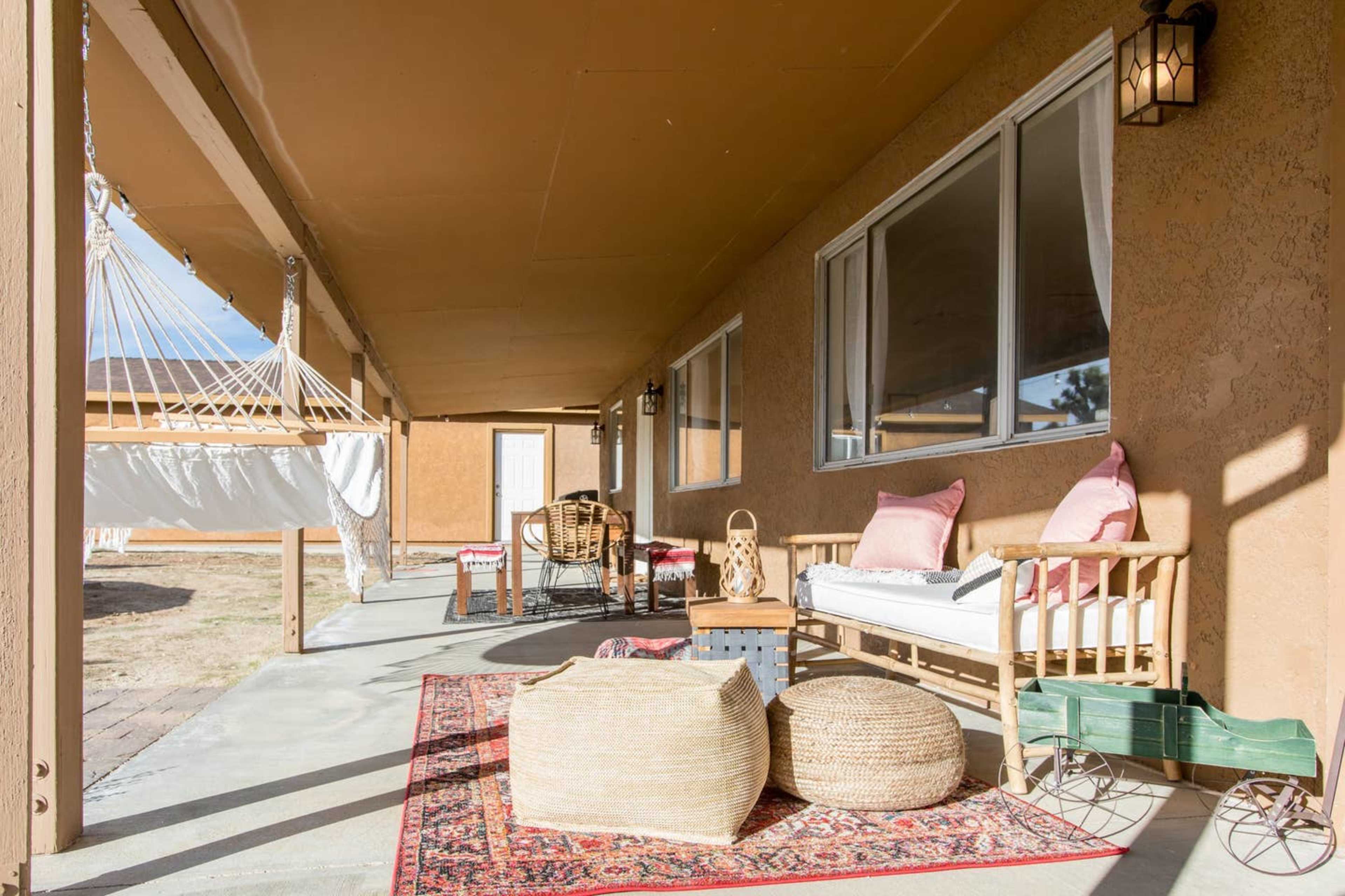 The image shows a covered patio with seating, a rug, and a hammock in the background.