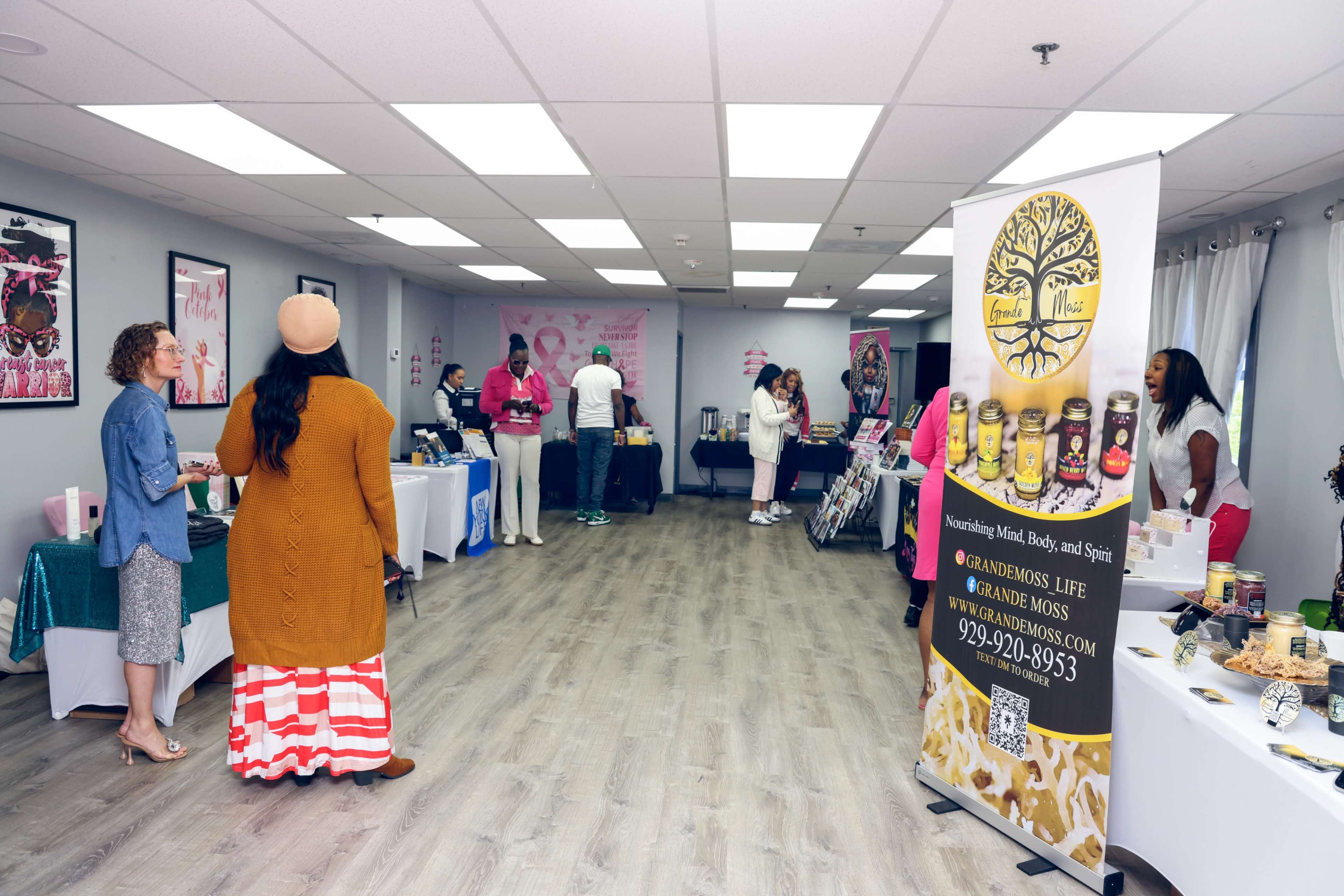 The image shows a brightly lit indoor market with various booths displaying products, and several people engaged in conversation and shopping.