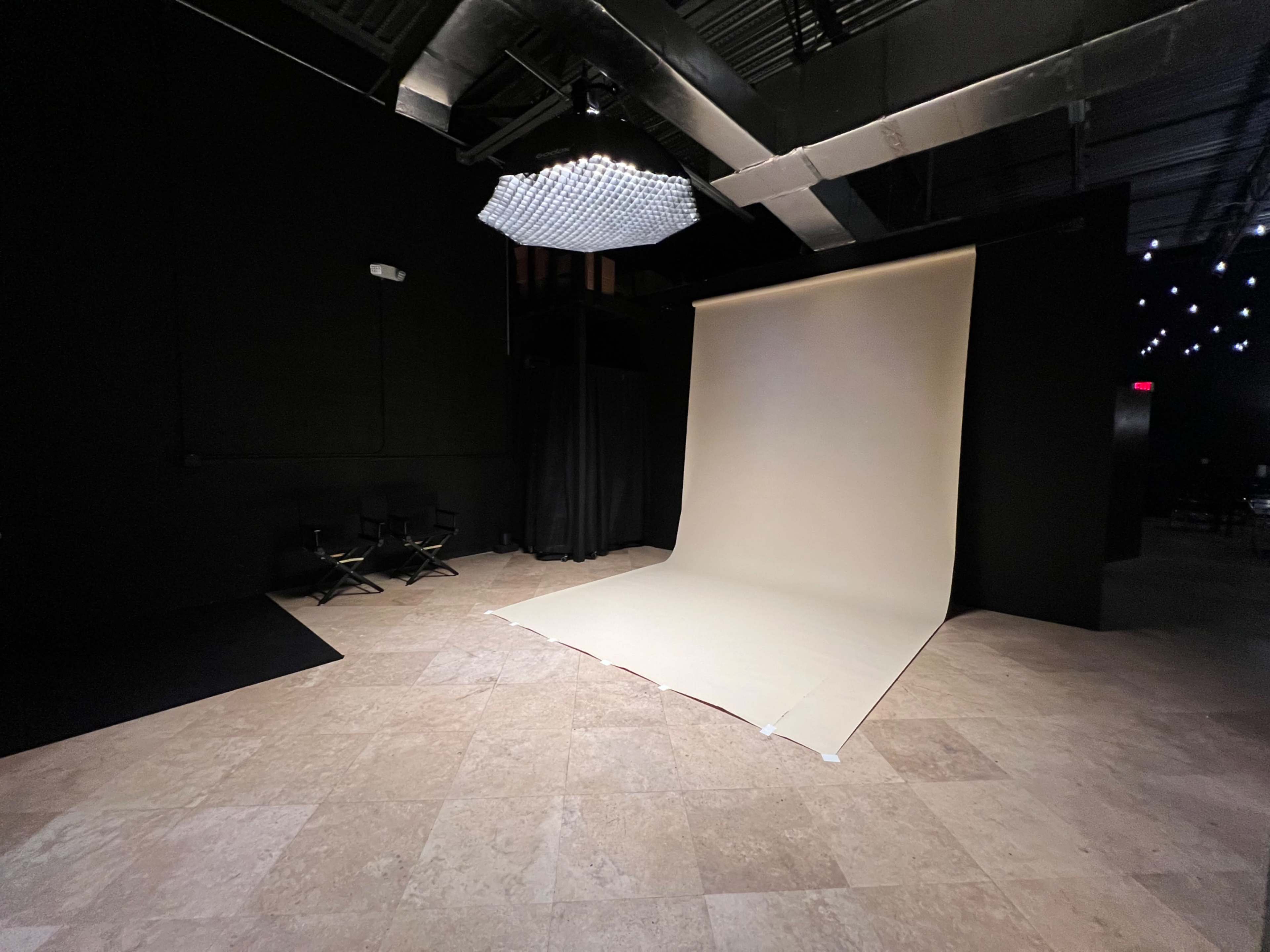 A photography studio with a light-colored backdrop, black walls, and a spotlight above.