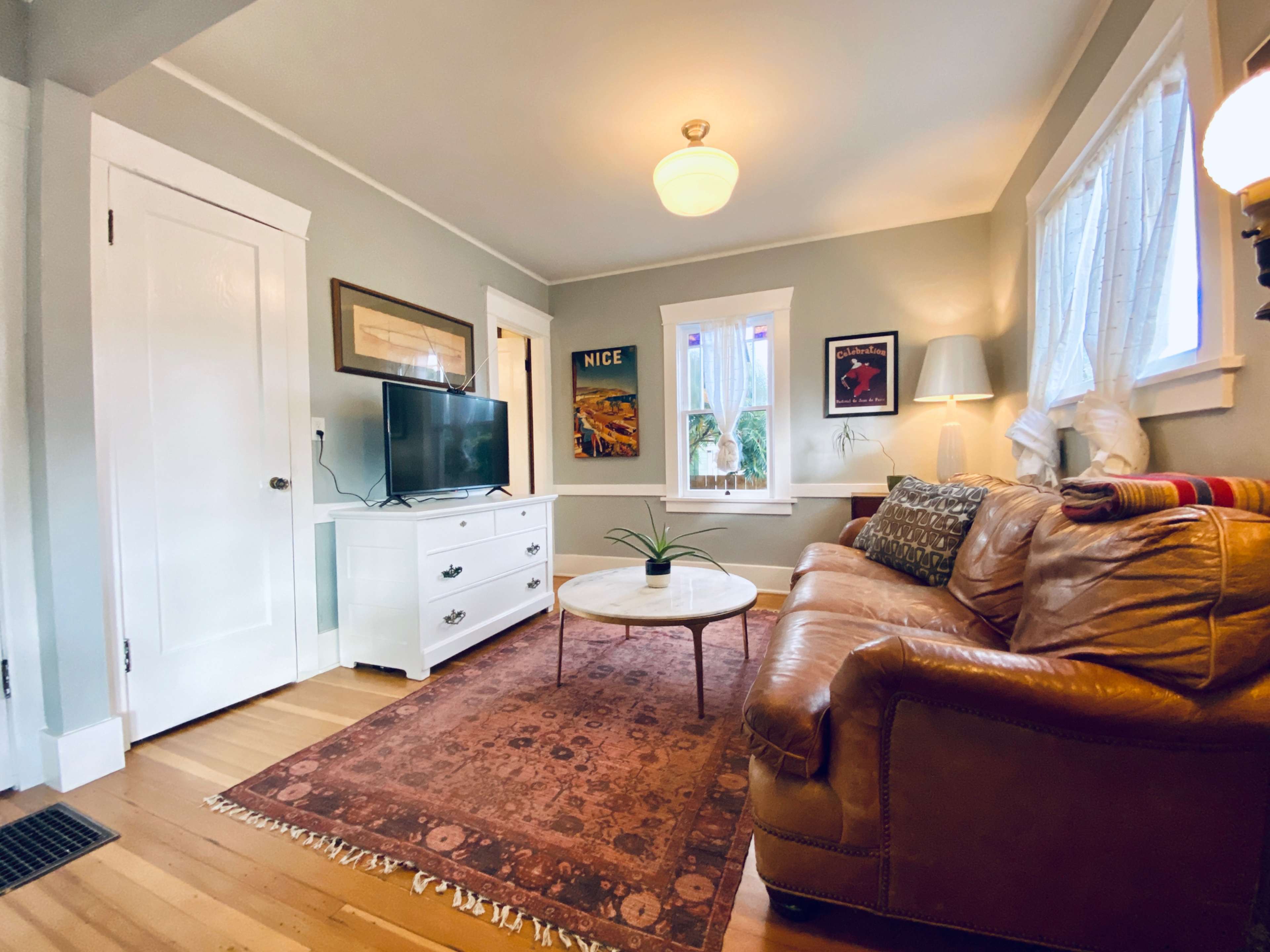 The image shows a living room with a brown leather sofa, a white television stand, and a circular coffee table on a patterned rug.