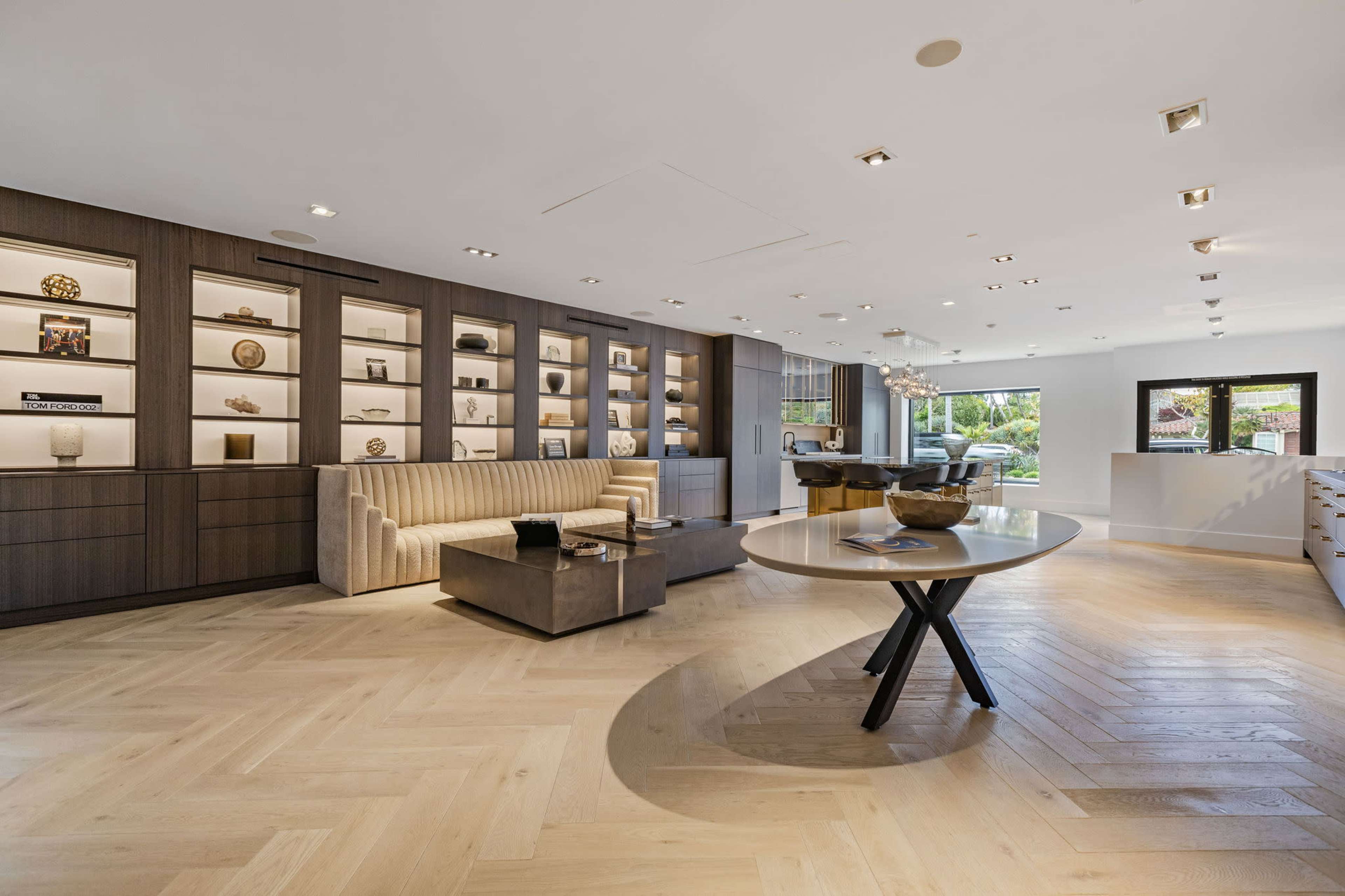 A spacious, modern interior featuring a wooden floor, a seating area with a sofa, and shelves displaying decorative items against a dark wooden wall.