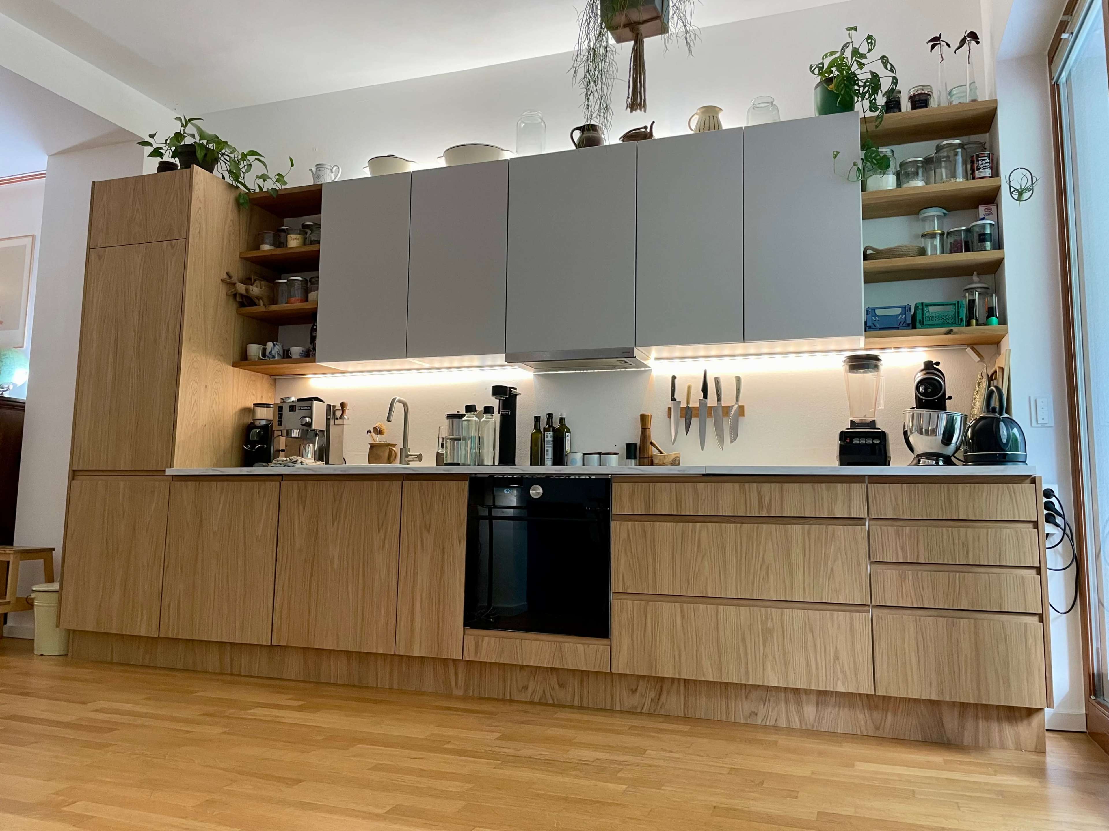 A modern kitchen features wooden cabinetry, gray upper cabinets, and various kitchen appliances displayed on open shelves.