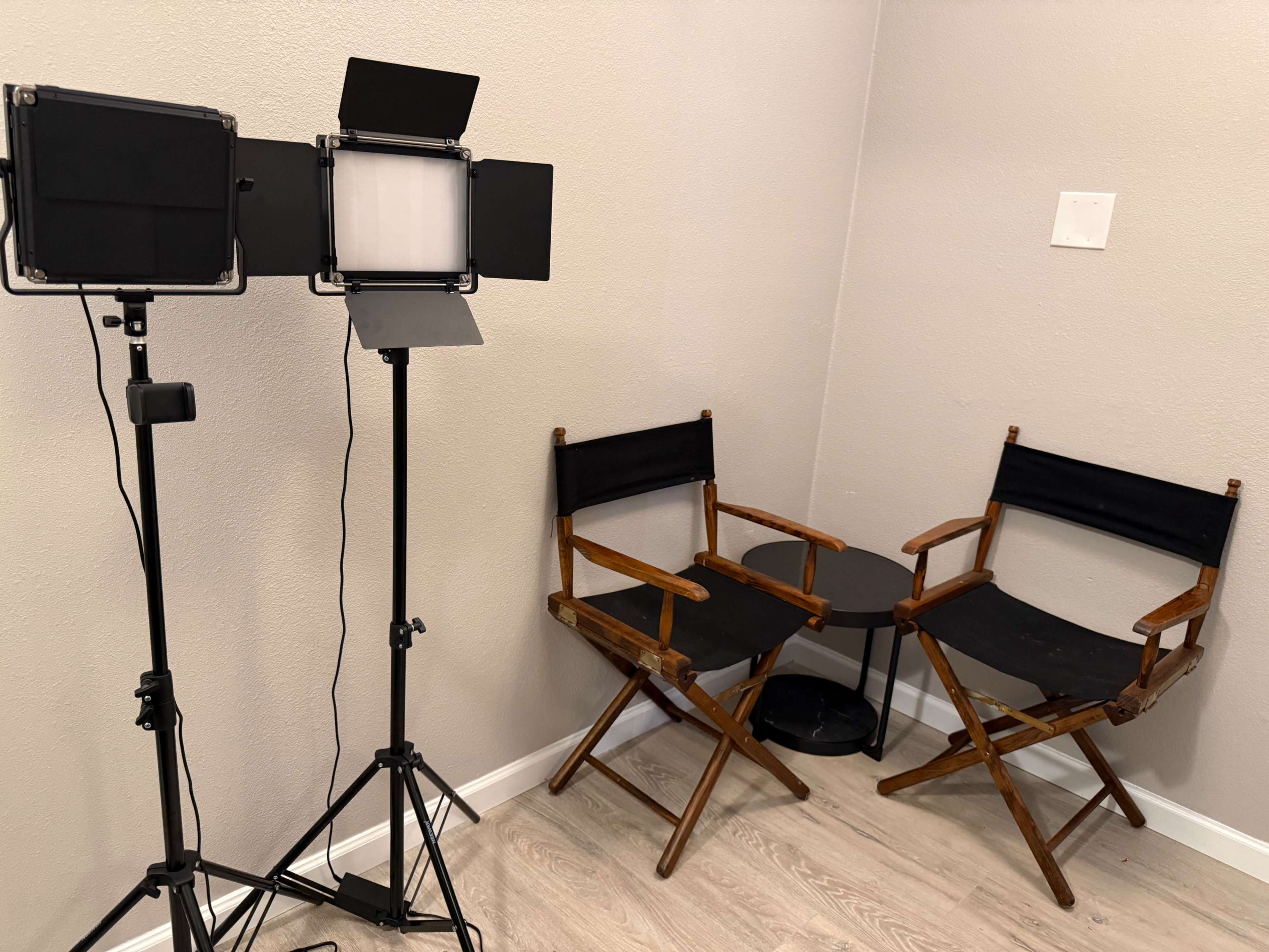 The image shows two wooden director's chairs positioned near a corner with lighting equipment set up.