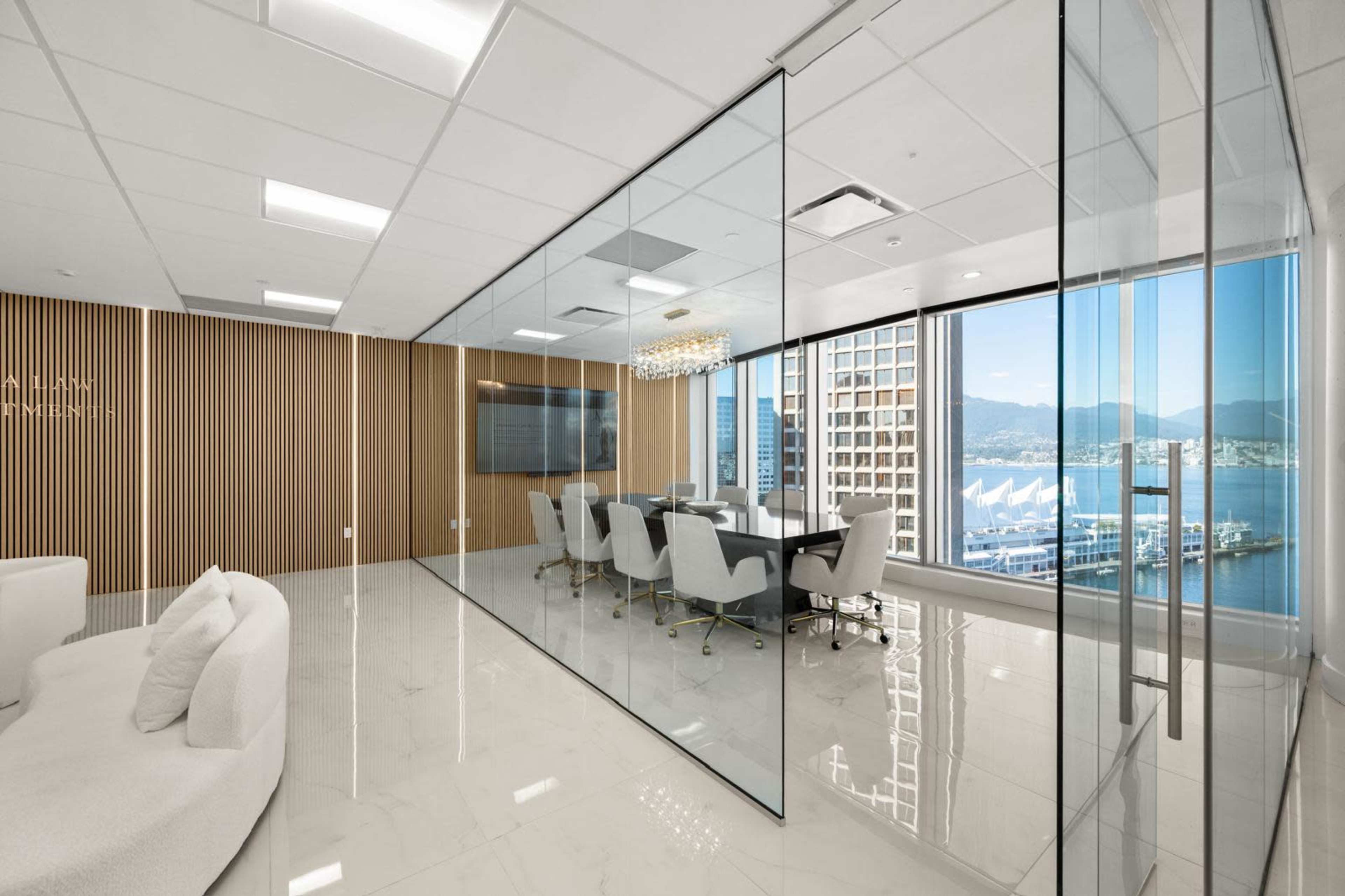 The image depicts a modern office space featuring a glass-walled conference room with a view of a waterfront marina and mountains.