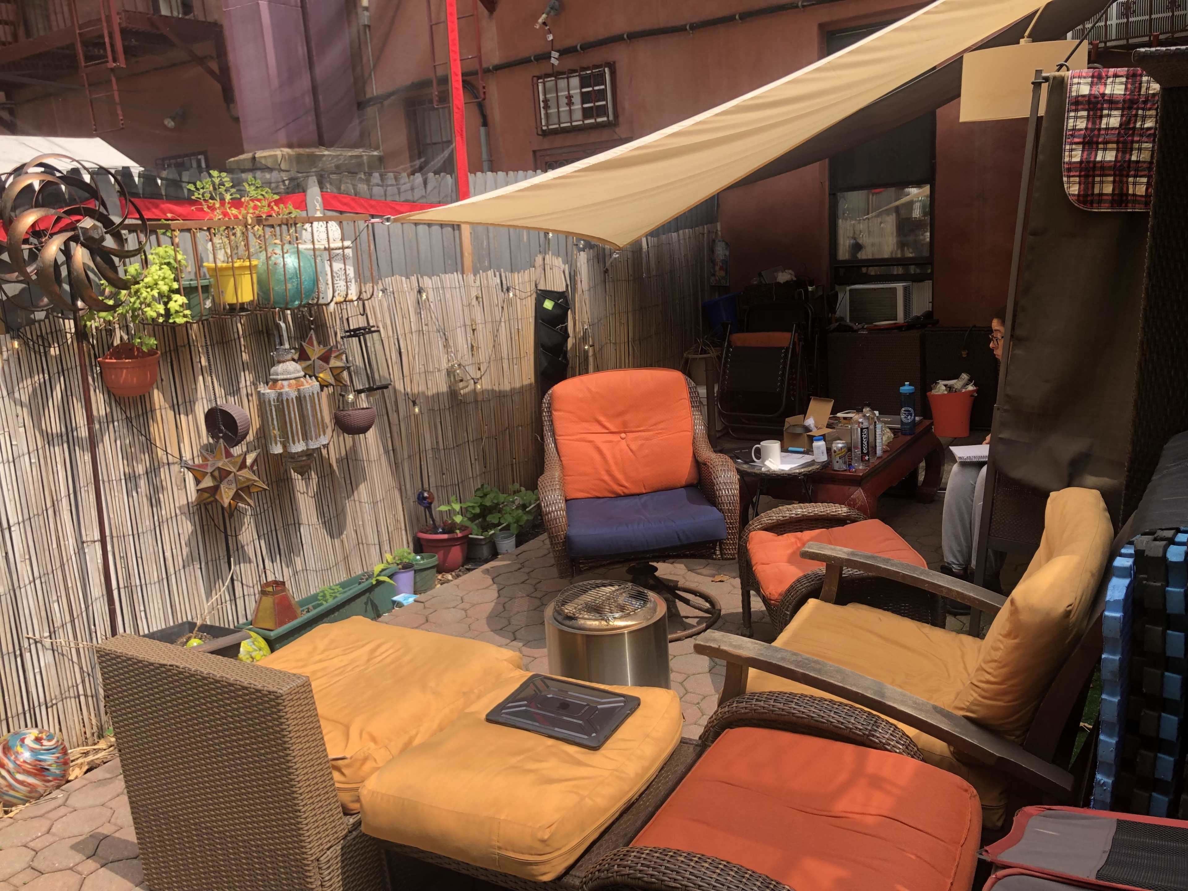 A backyard patio area with wicker furniture, a fire pit, and various plants and decorations.