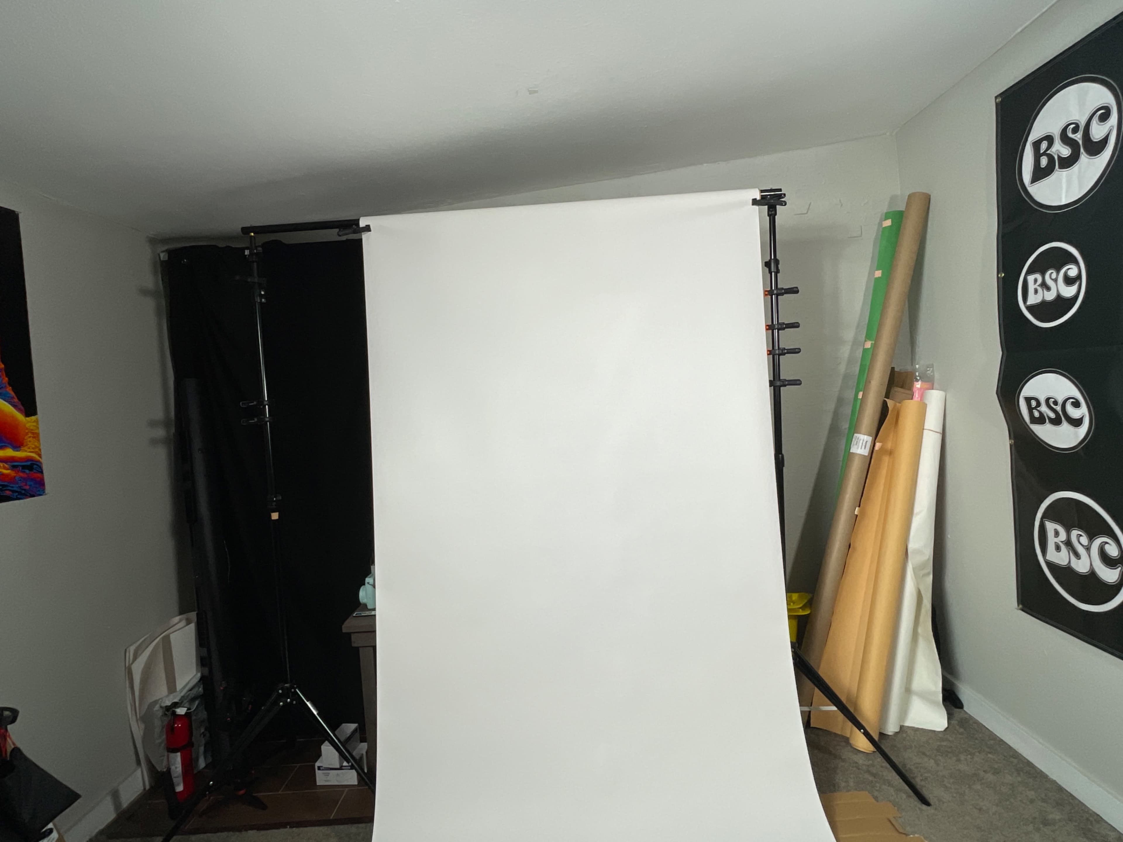 A photography setup with a white backdrop, light stands, and various rolls of paper in a corner of a room.