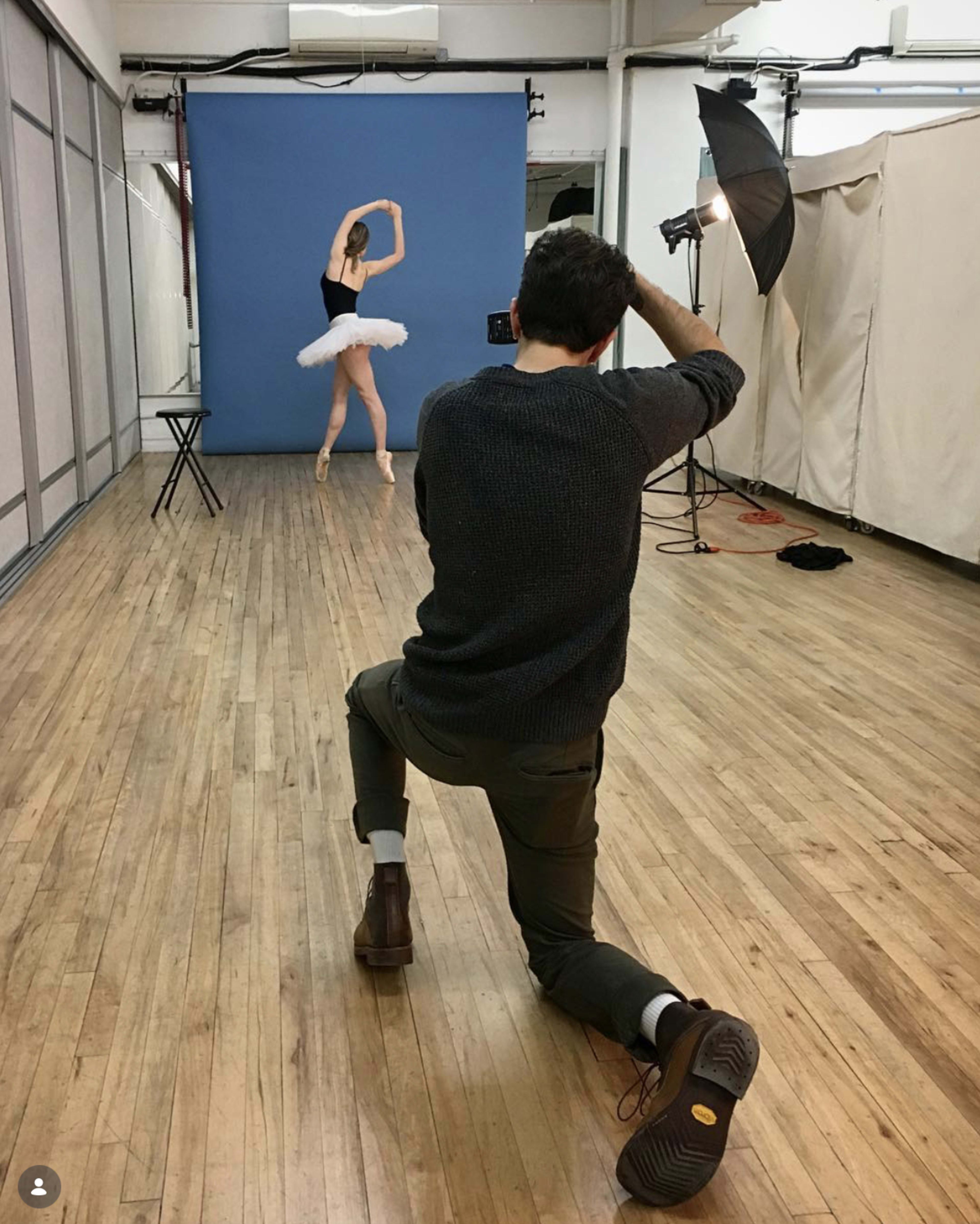 A photographer captures a ballet dancer posing against a blue backdrop in an indoor studio.