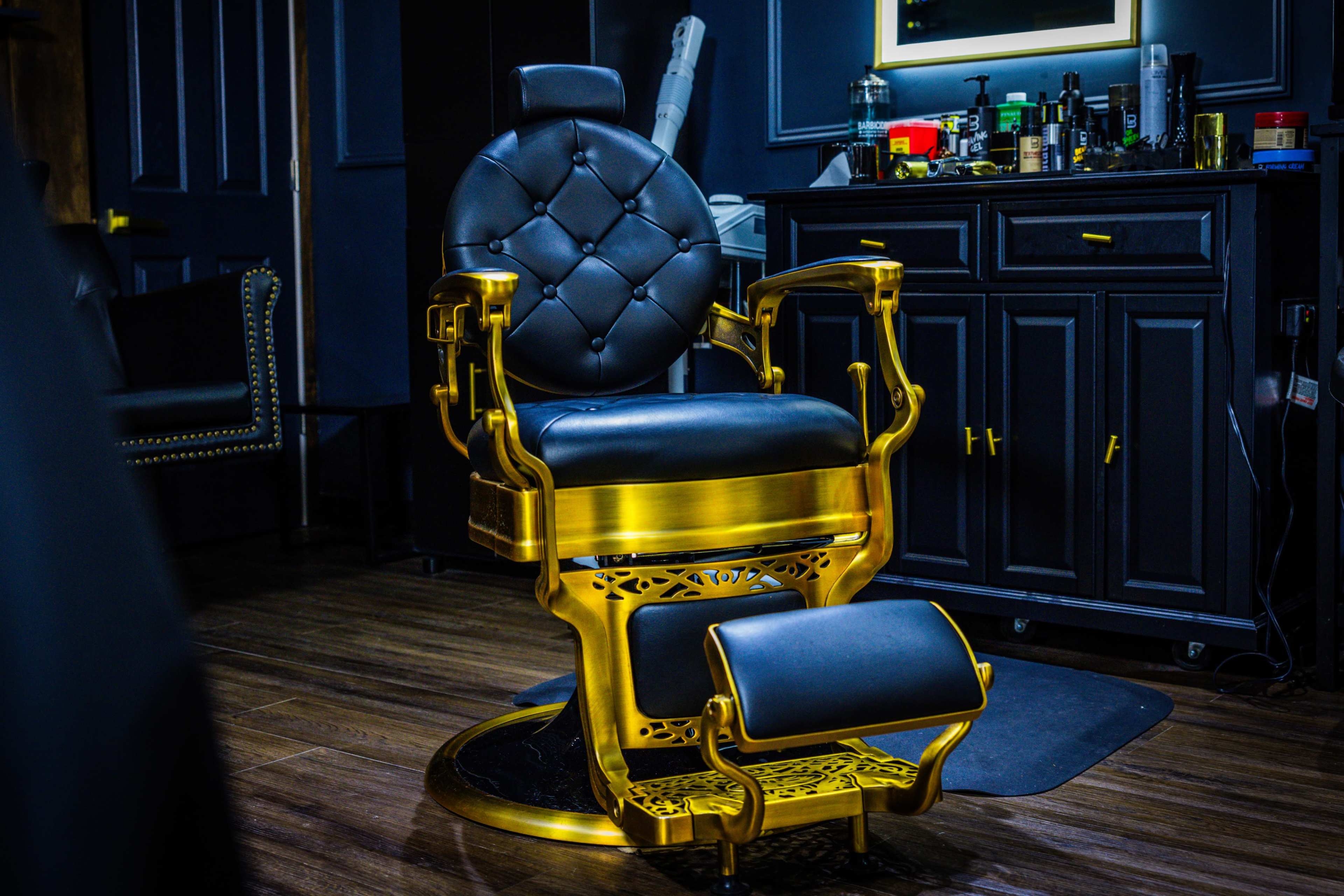The image shows a luxurious golden barber chair with black upholstery in a modern barber shop setting.