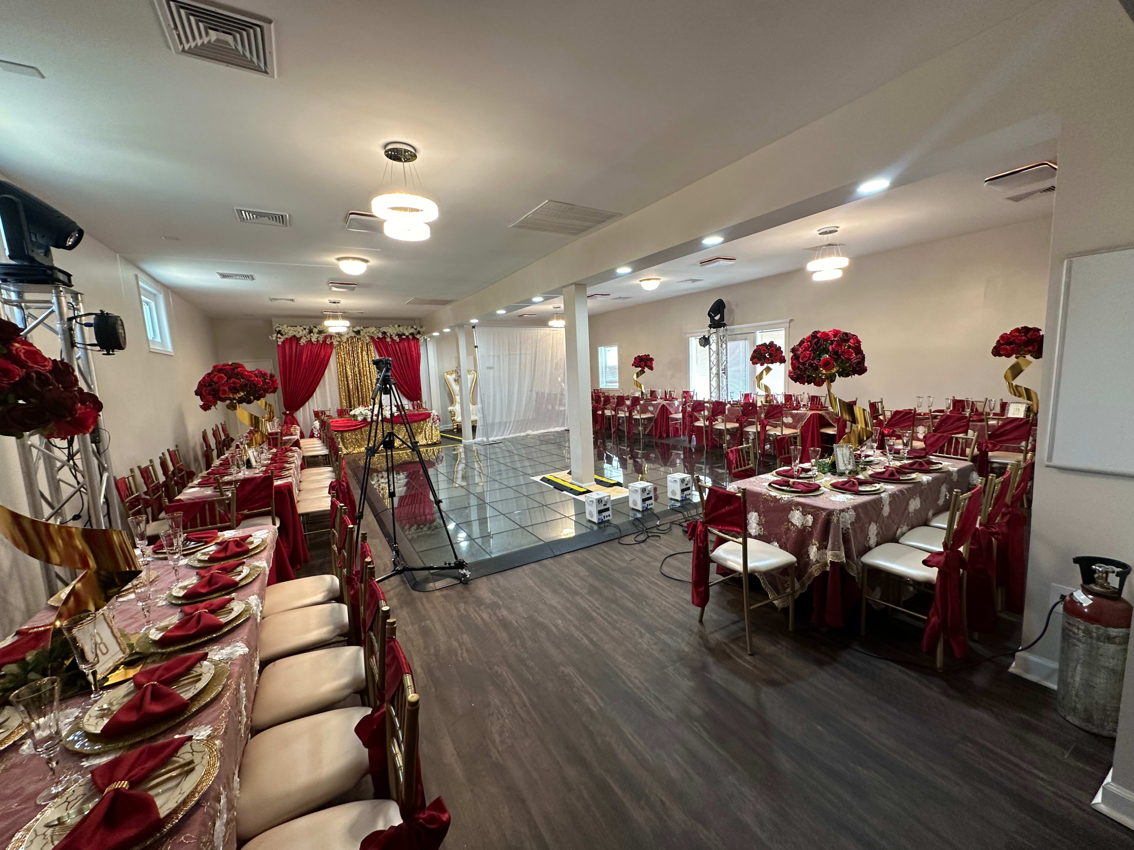 A banquet hall is set up for an elegant event, featuring tables adorned with red and gold decorations and floral centerpieces.