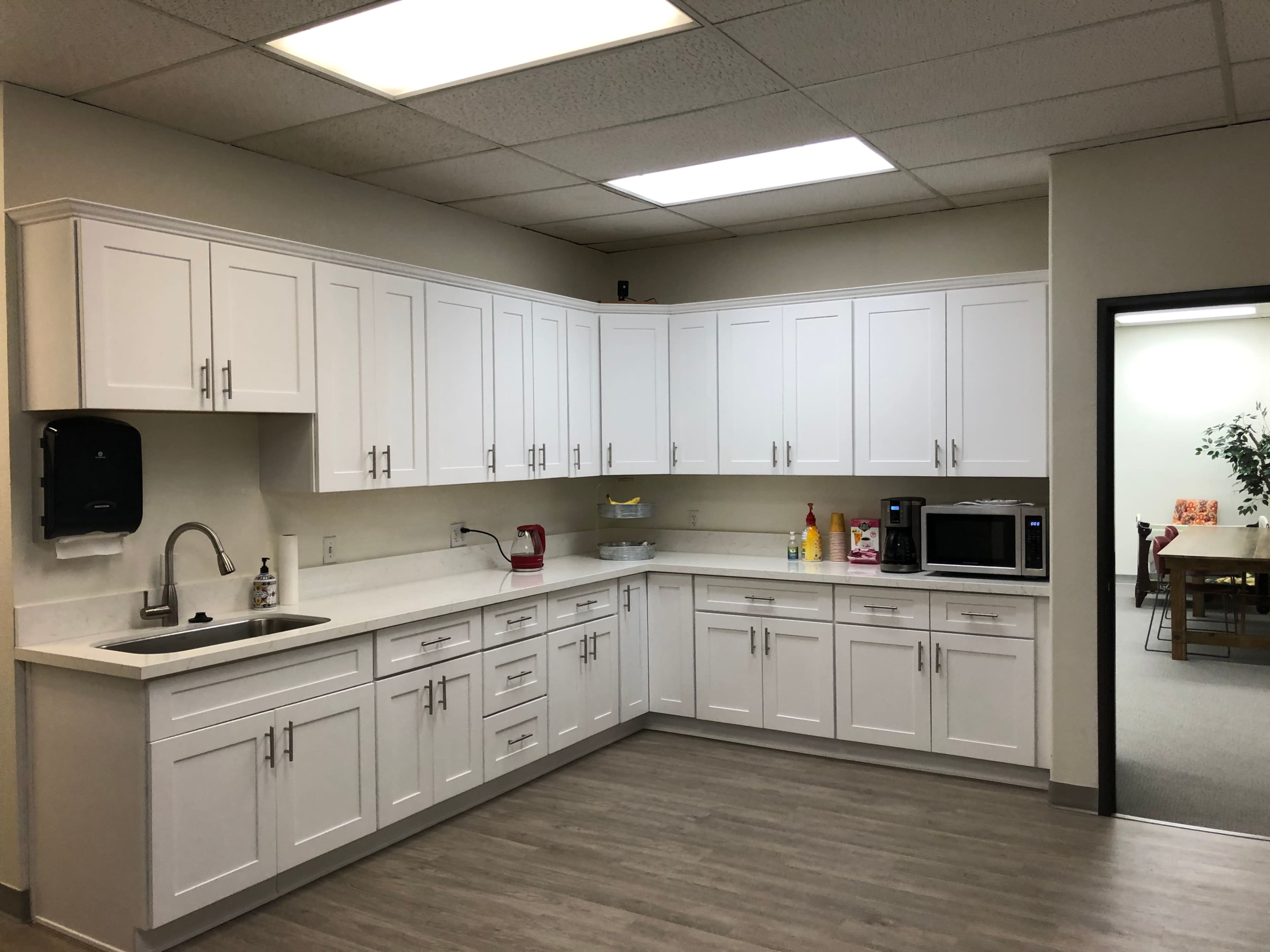 A modern kitchen space with white cabinets, a sink, a microwave, and various appliances neatly arranged.
