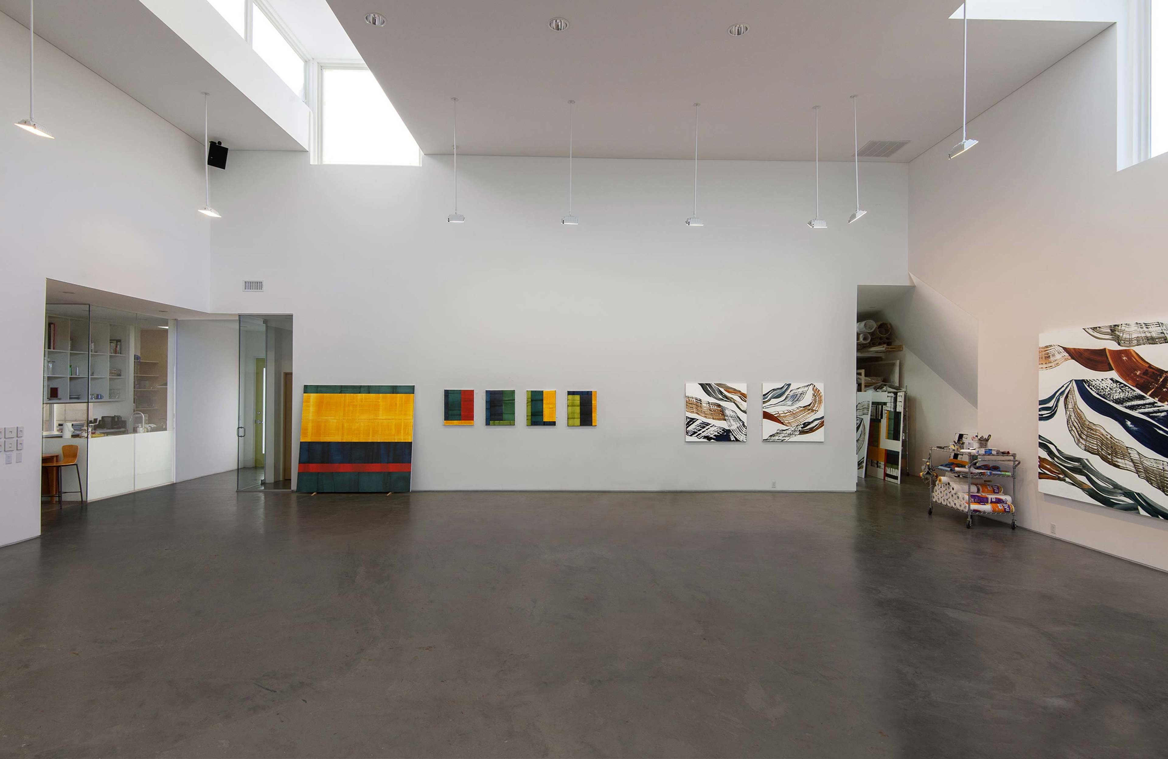 A modern art gallery with high ceilings, featuring abstract paintings on the walls and a polished concrete floor.