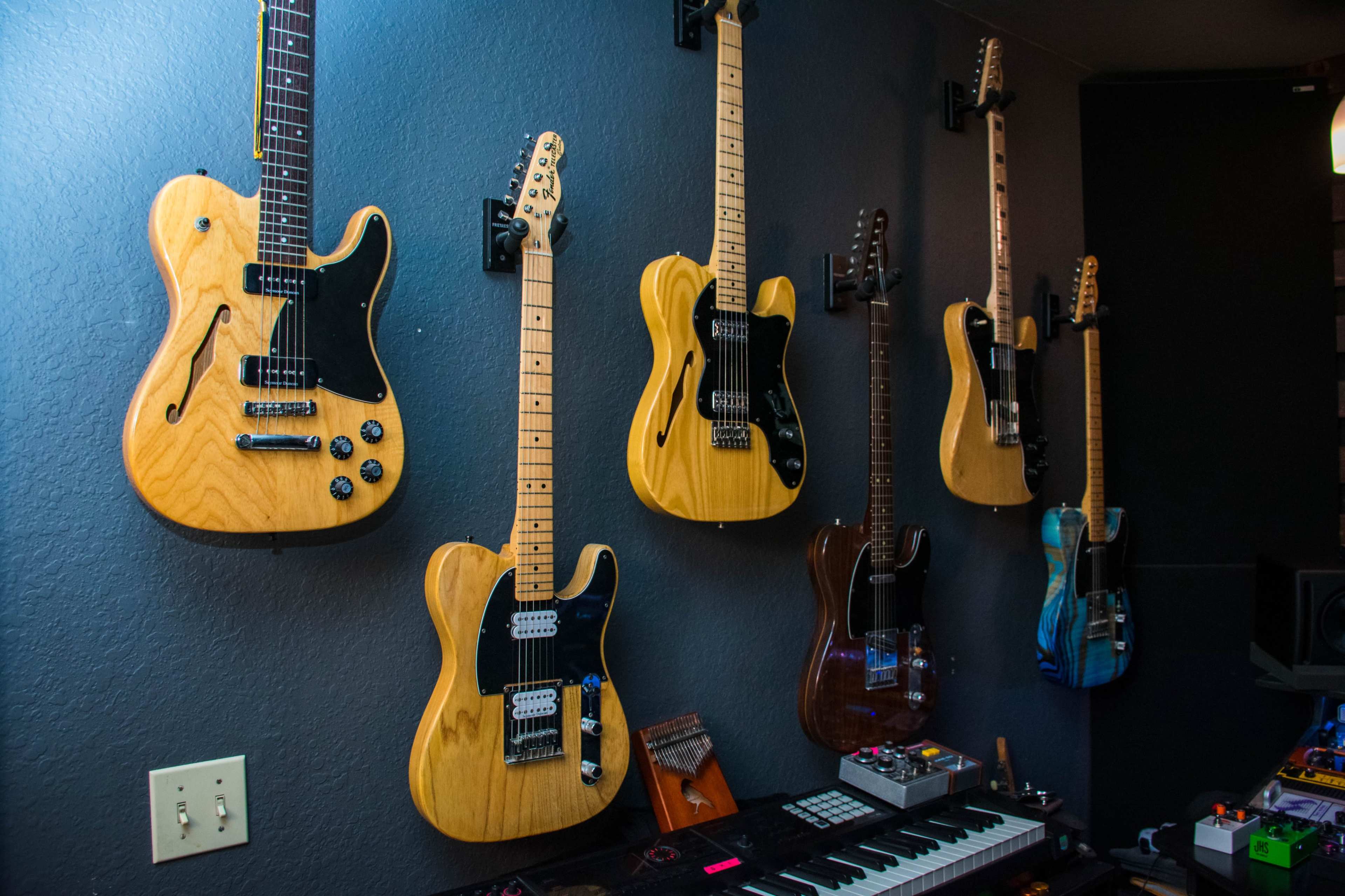 The image shows a wall displaying a collection of seven electric guitars in various styles mounted alongside a keyboard and music equipment.