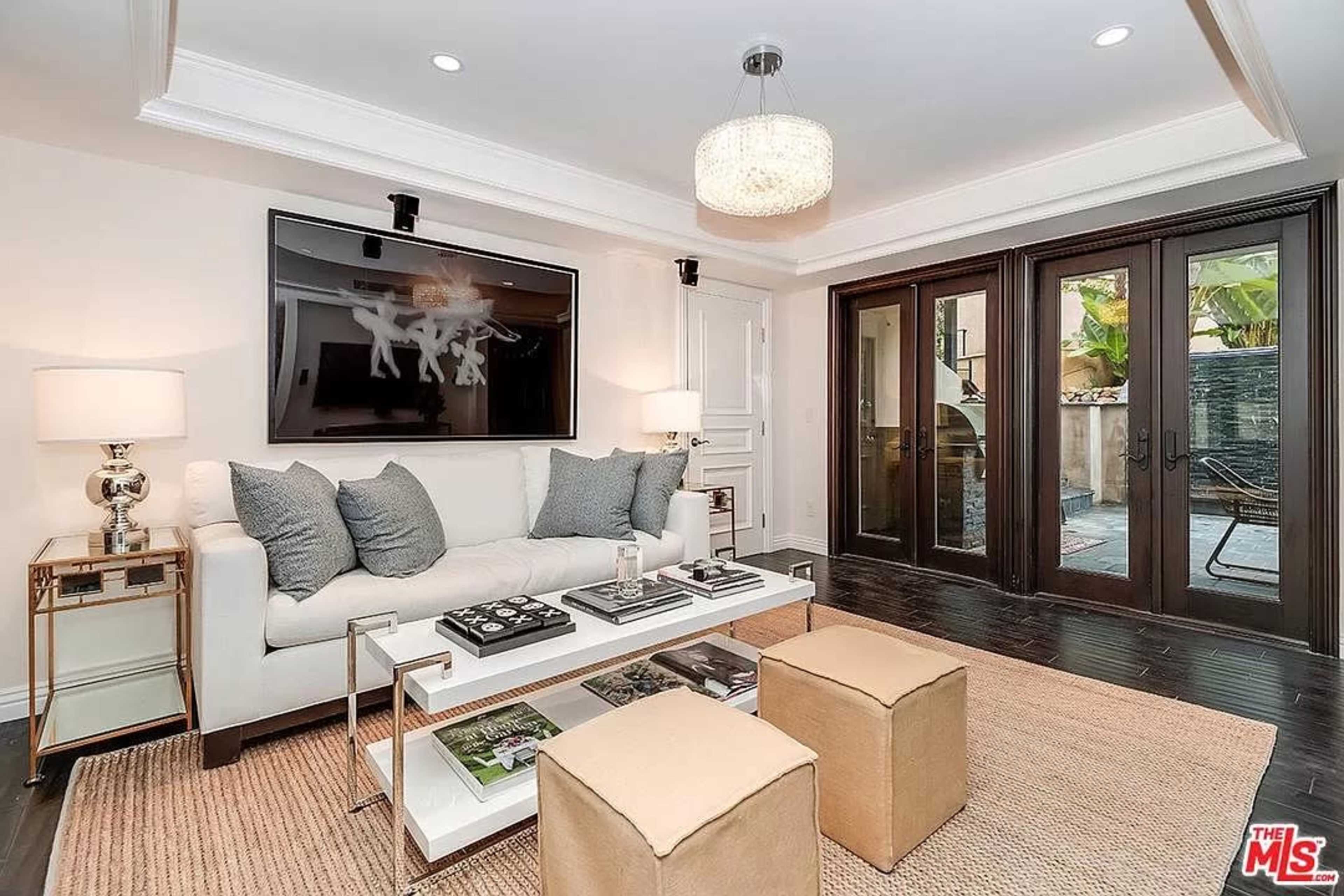 A modern living room features a white sofa with gray cushions, a glass coffee table, and double doors leading to an outdoor space.