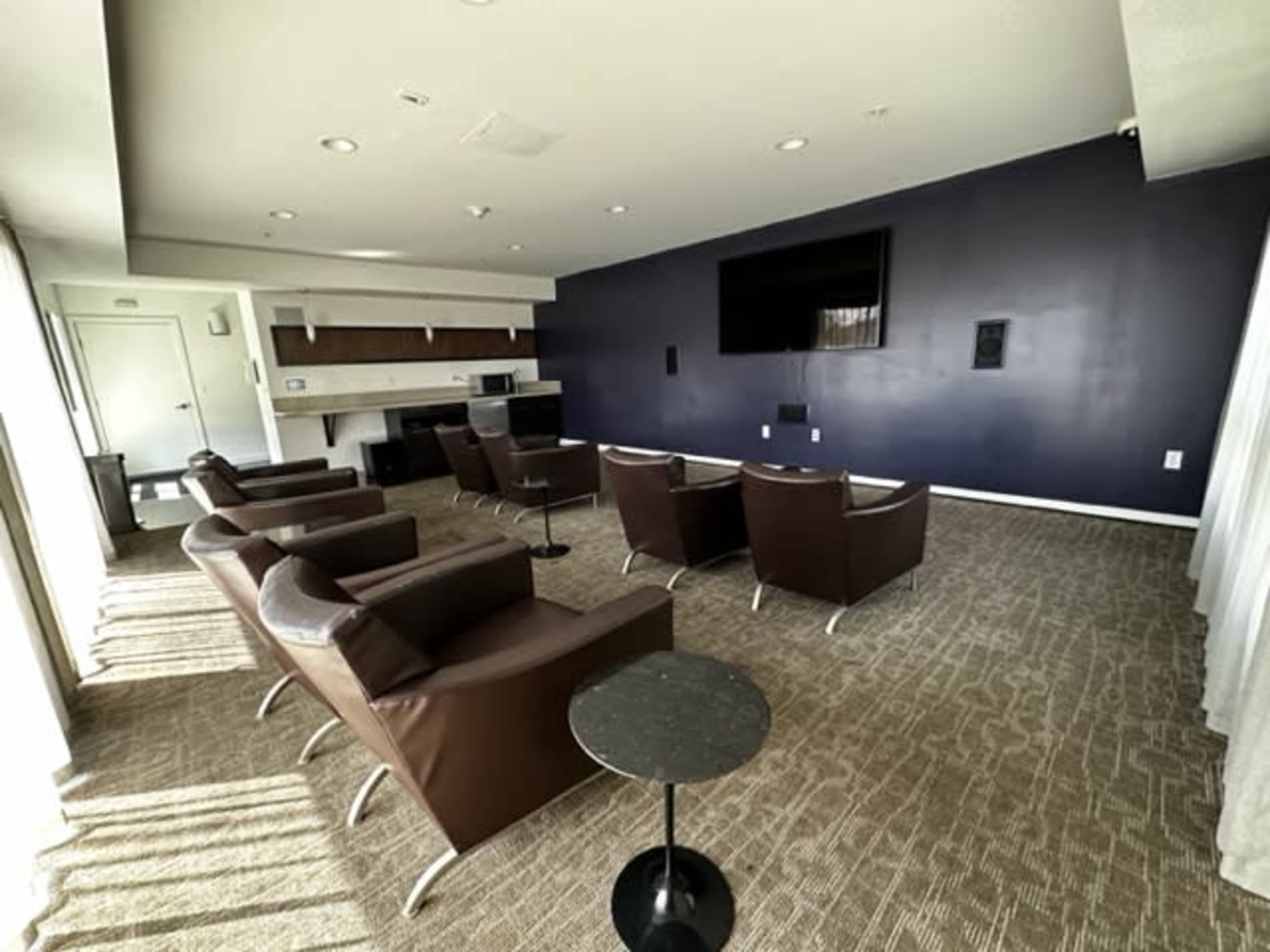A spacious lounge area with several brown leather chairs arranged in front of a wall-mounted television and a small side table.