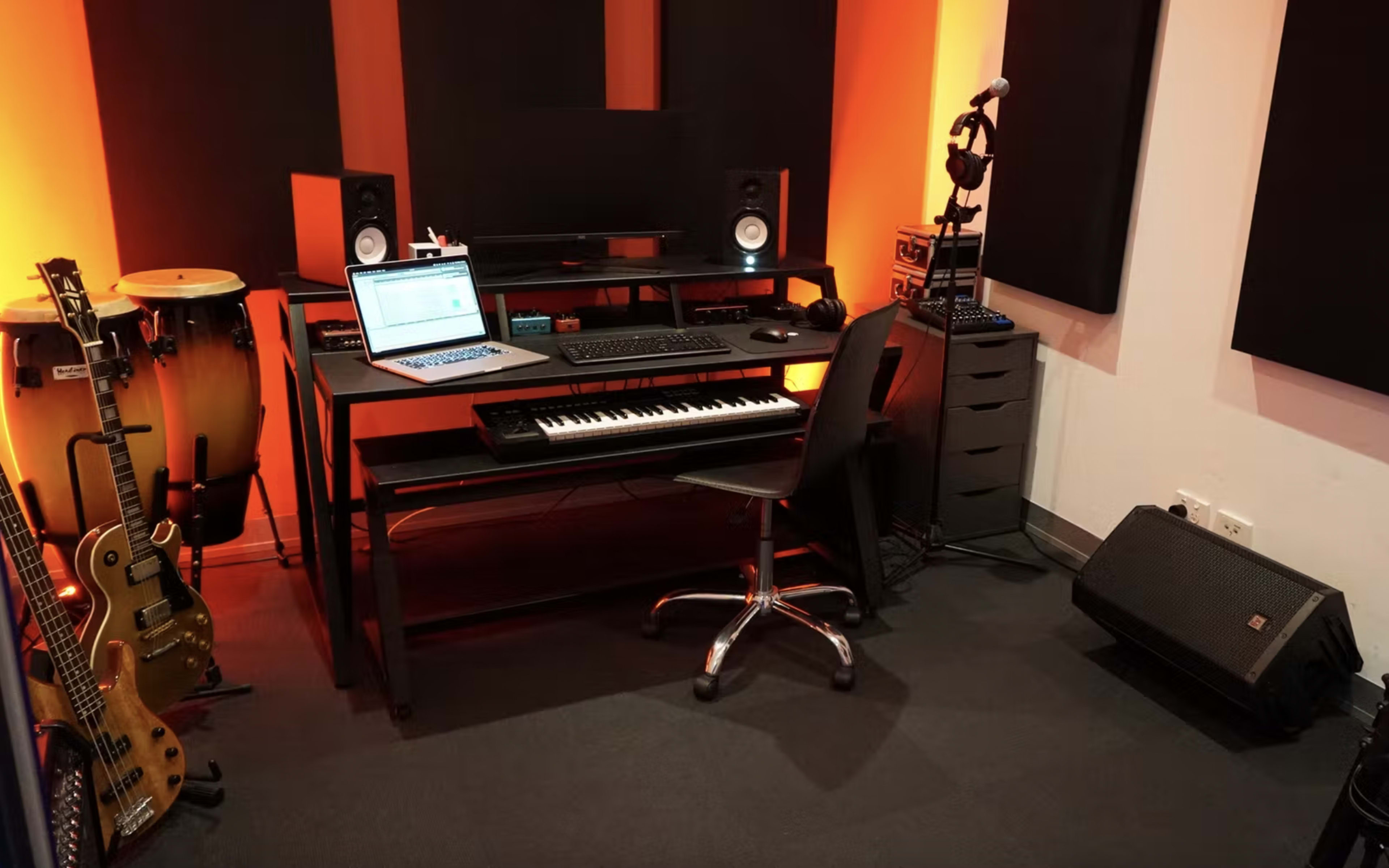 A music studio with a keyboard, computer, speakers, microphones, guitars, and soundproof panels on the walls.