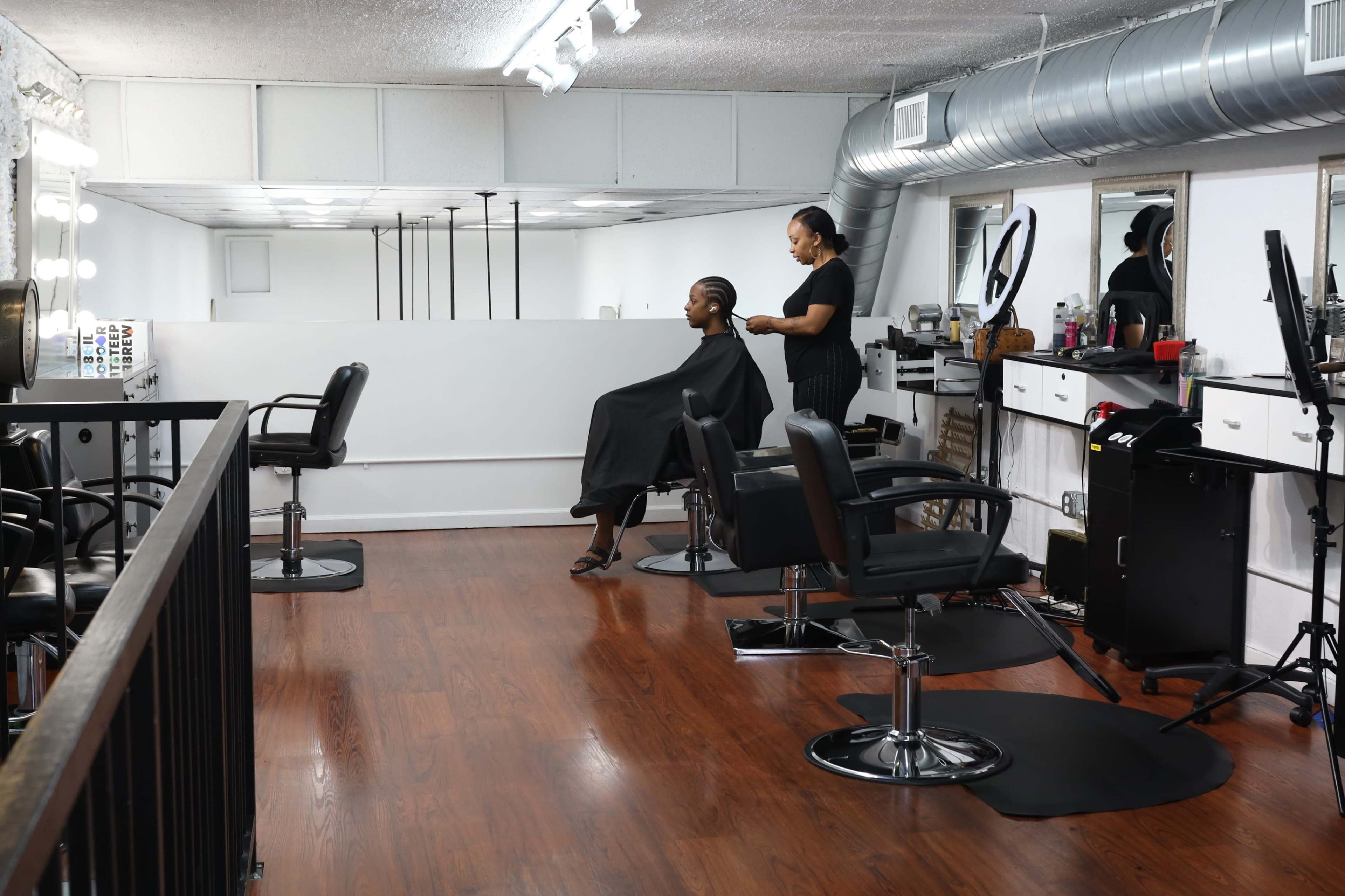 A hair salon features a stylist working on a client's hair while multiple styling stations are visible in the background.
