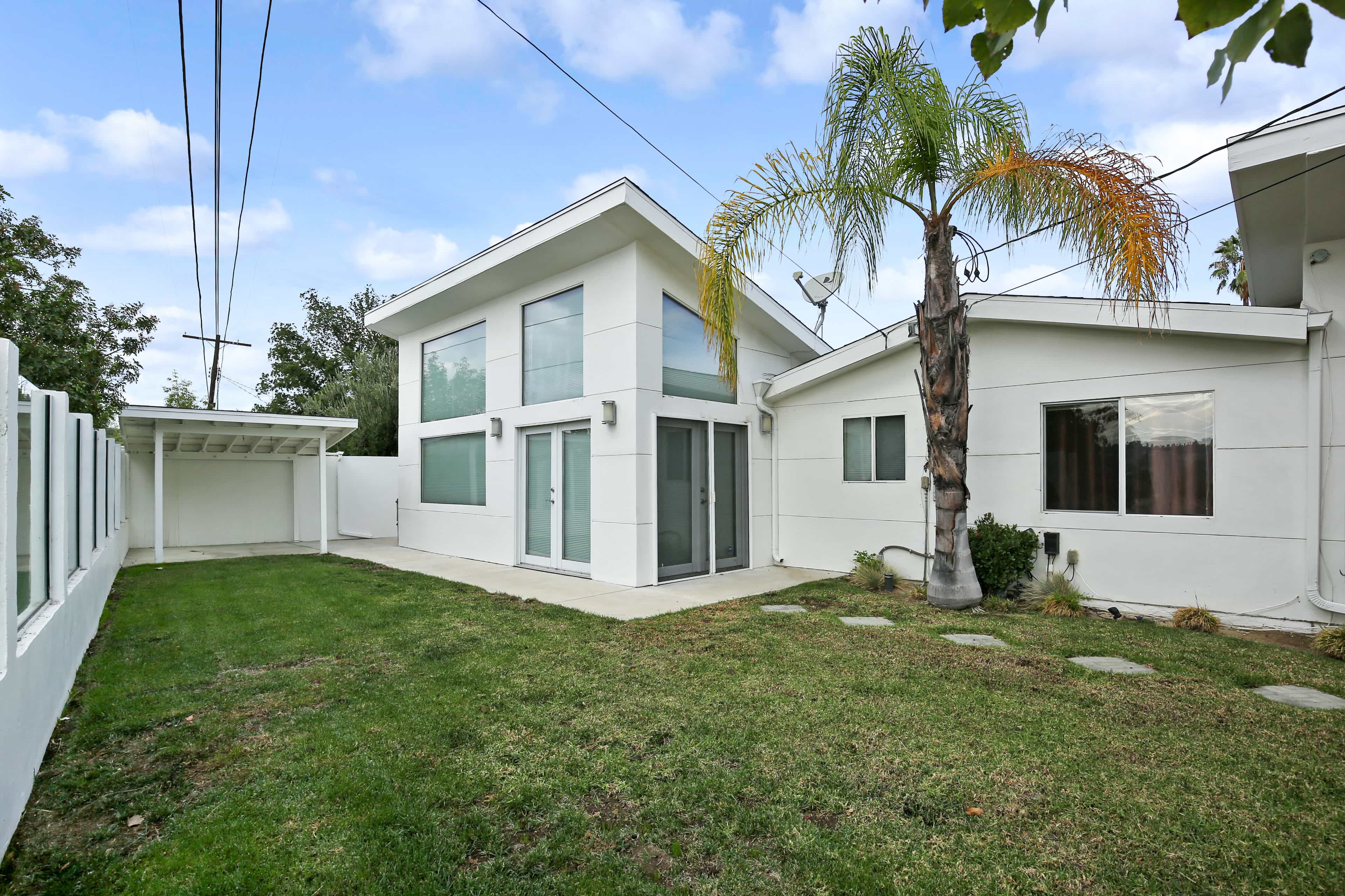 A modern two-story house with large windows, a manicured lawn, and a palm tree in the backyard.
