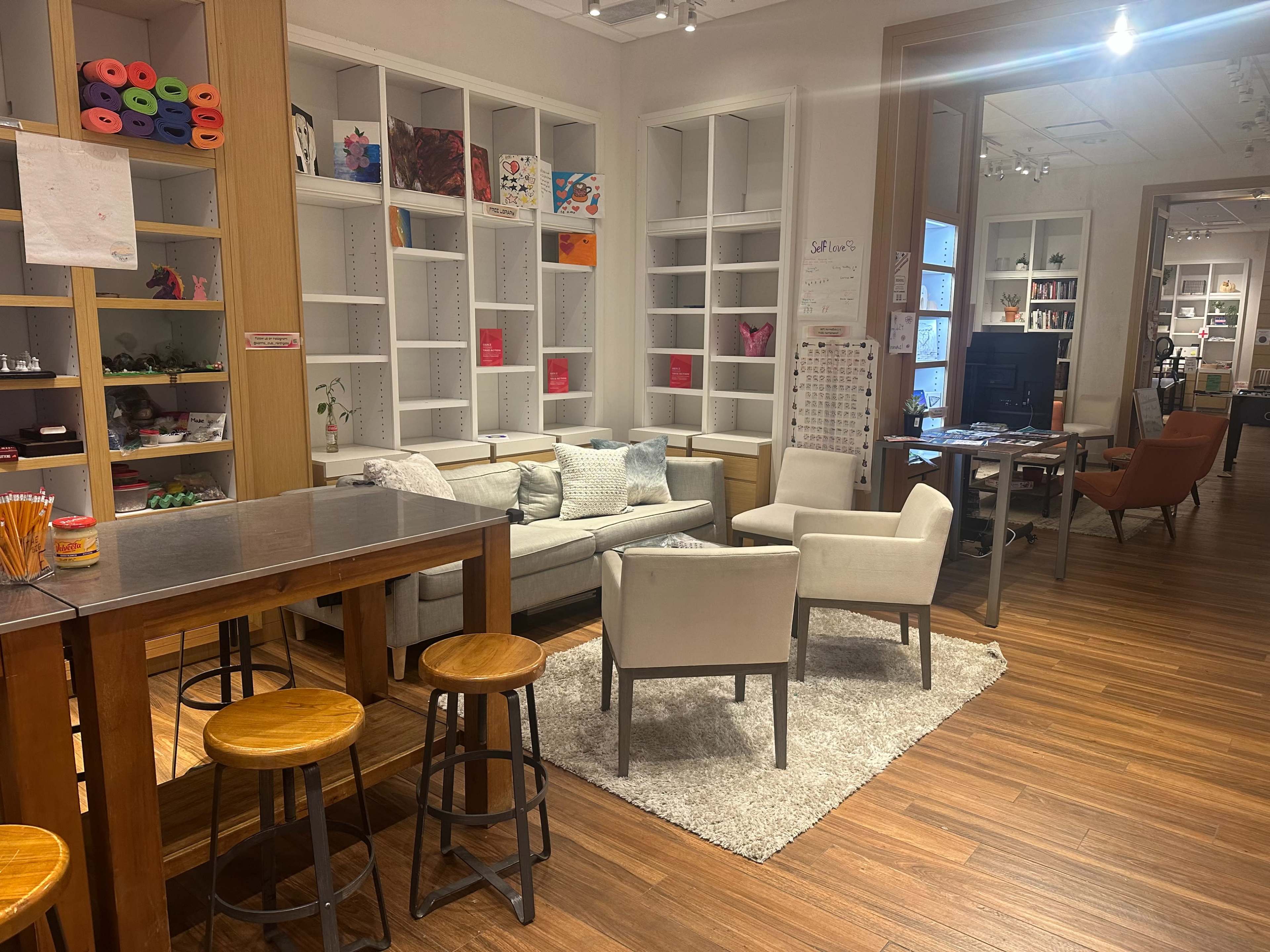 The image shows a cozy, well-lit room with a seating area consisting of a couch and two chairs, surrounded by bookshelves and a workspace with a computer.