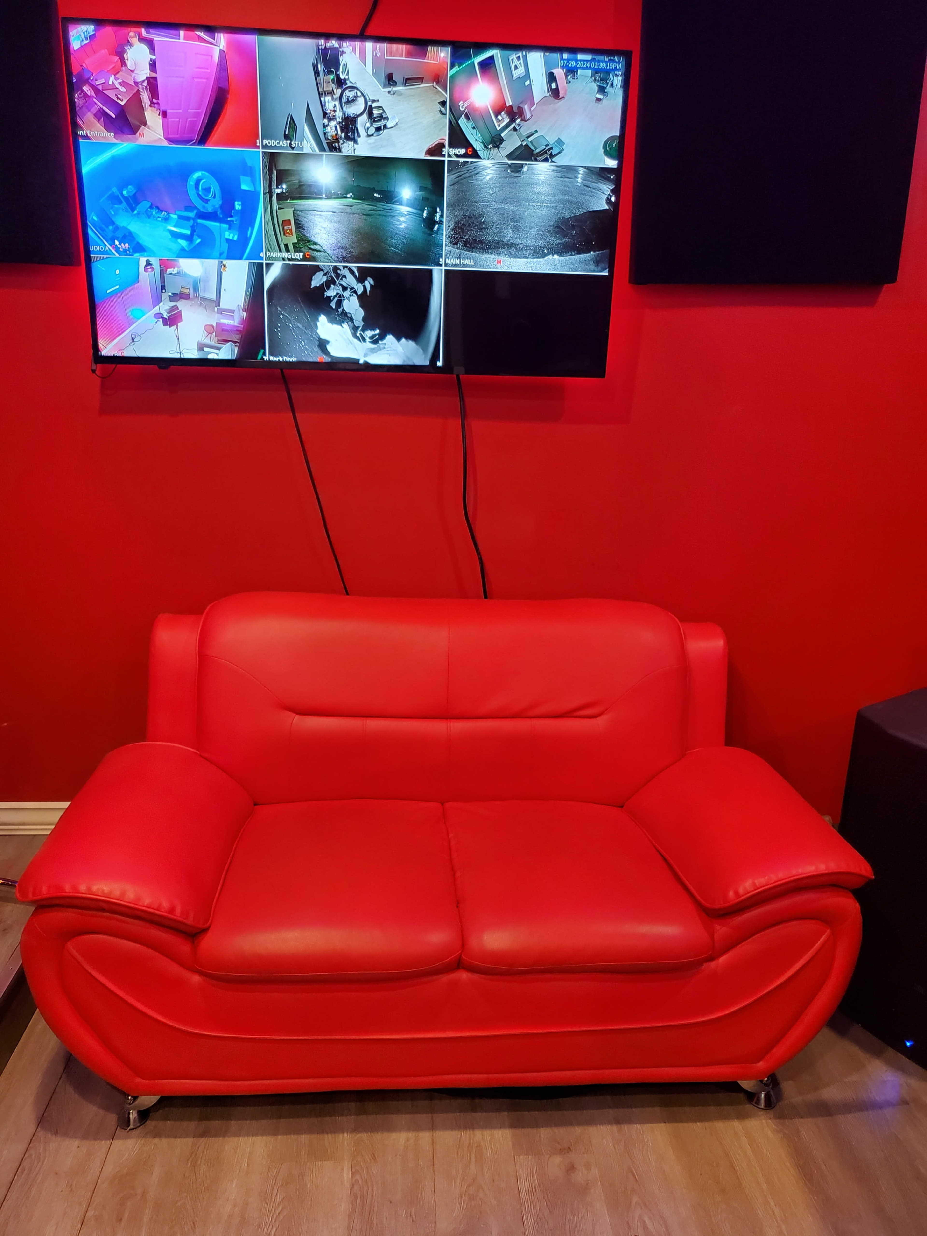A red sofa sits in front of a screen displaying multiple camera feeds on a red wall.