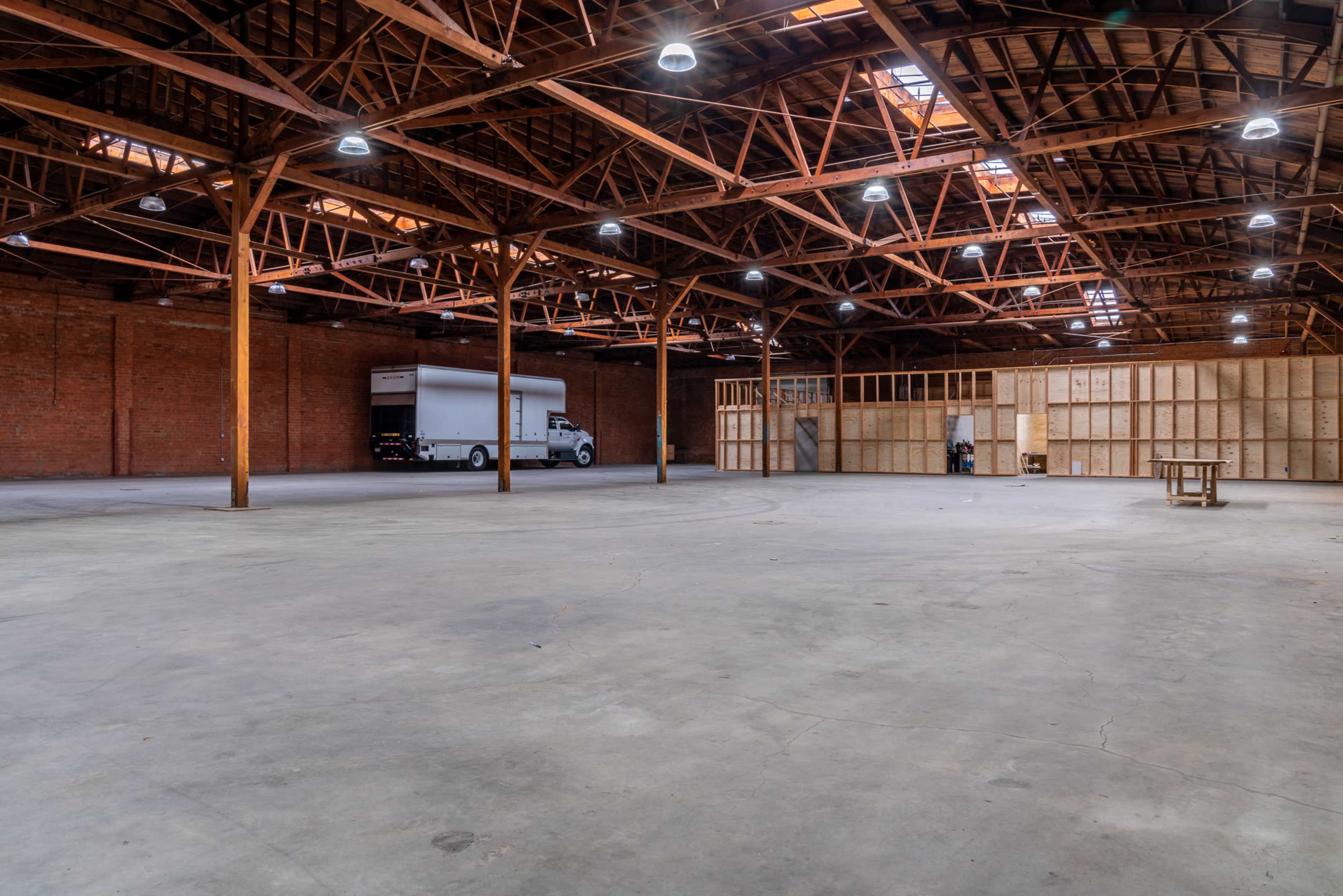 A spacious, empty warehouse with exposed wooden beams and a large truck parked near a partitioned area.