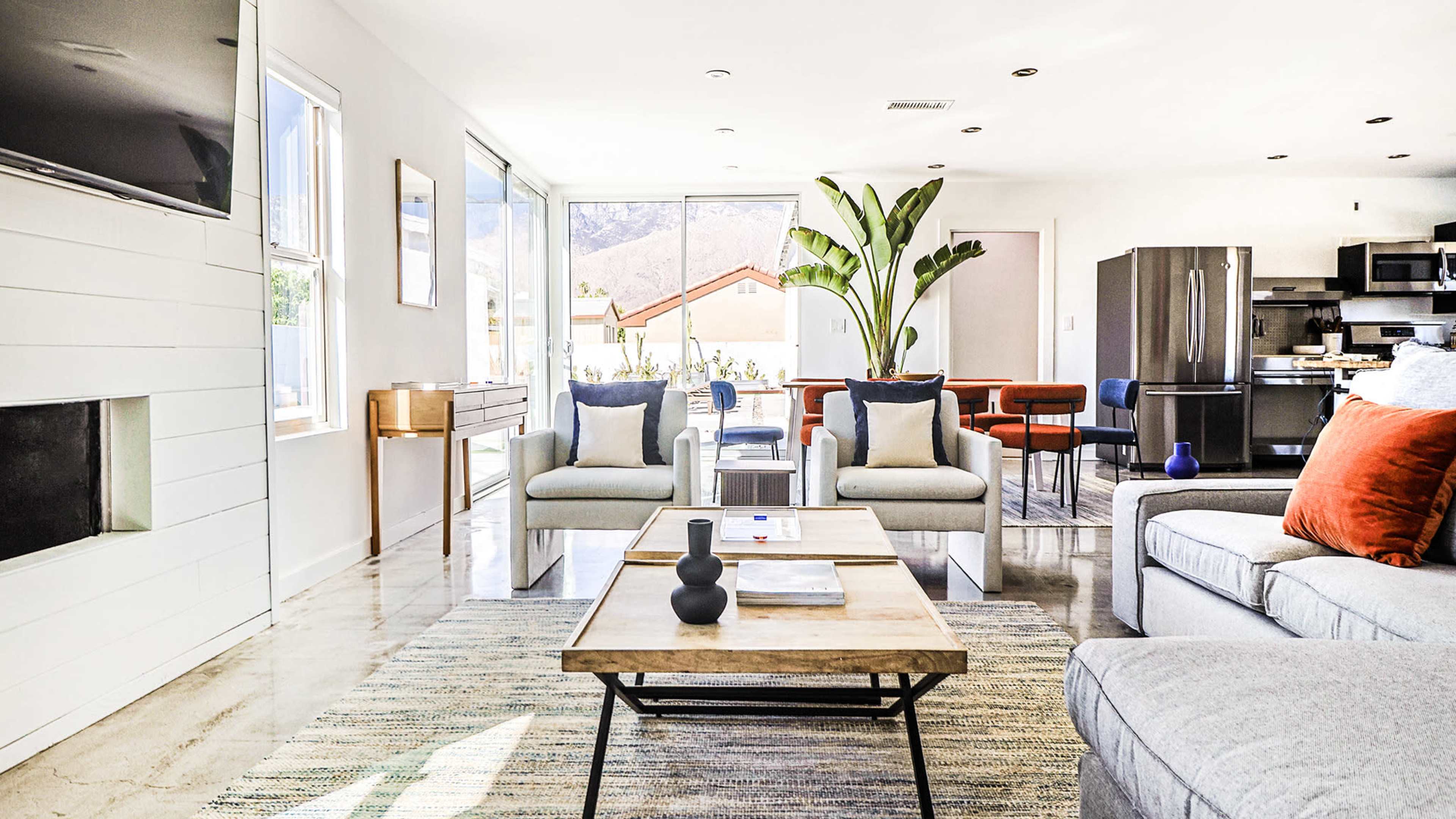 A contemporary living room featuring a light-colored sofa, a coffee table, and large windows with a view of the outside.