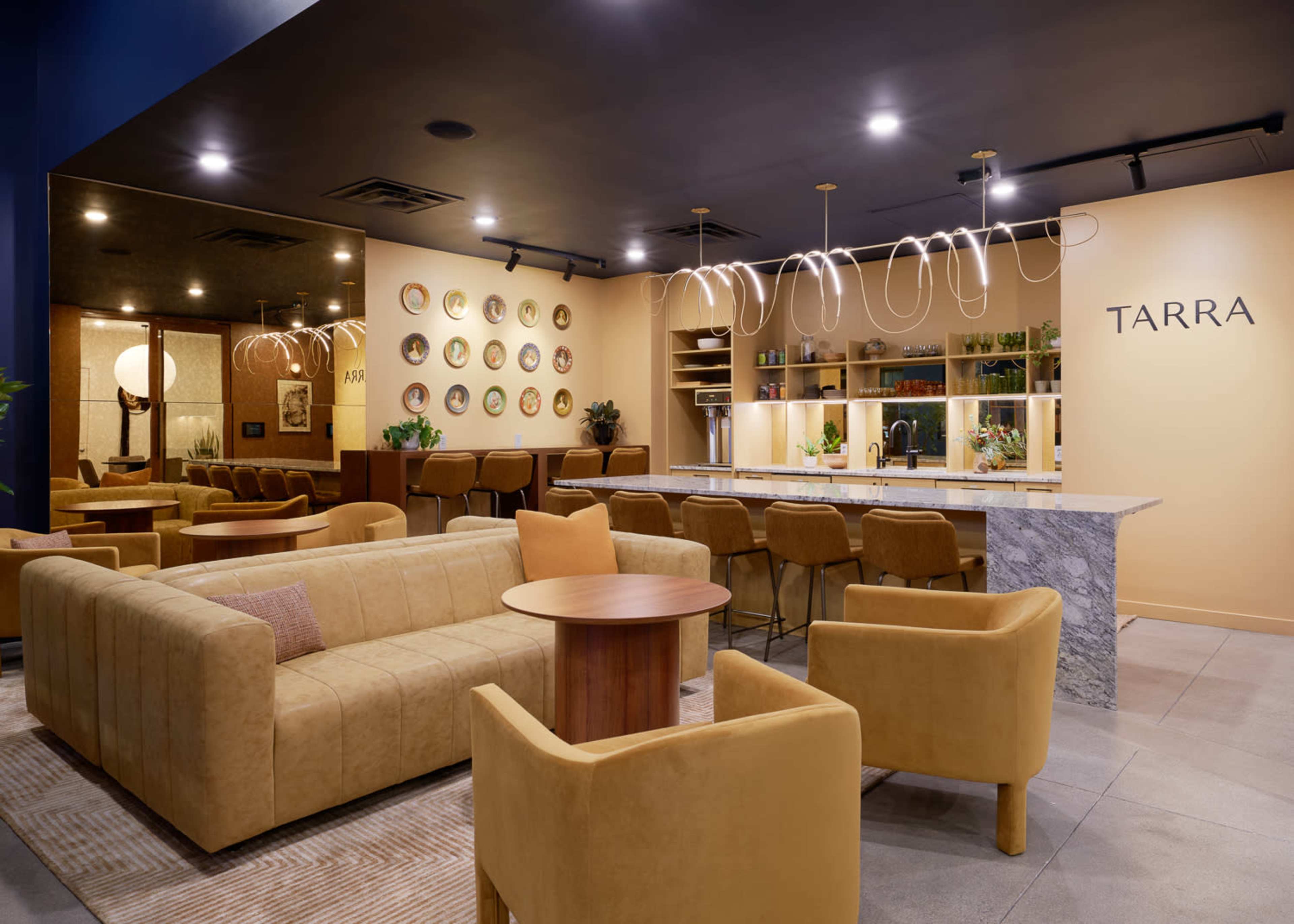 A modern lounge area with a yellow color scheme, featuring a large beige sofa, matching chairs, and a bar with decorative plates on the wall.