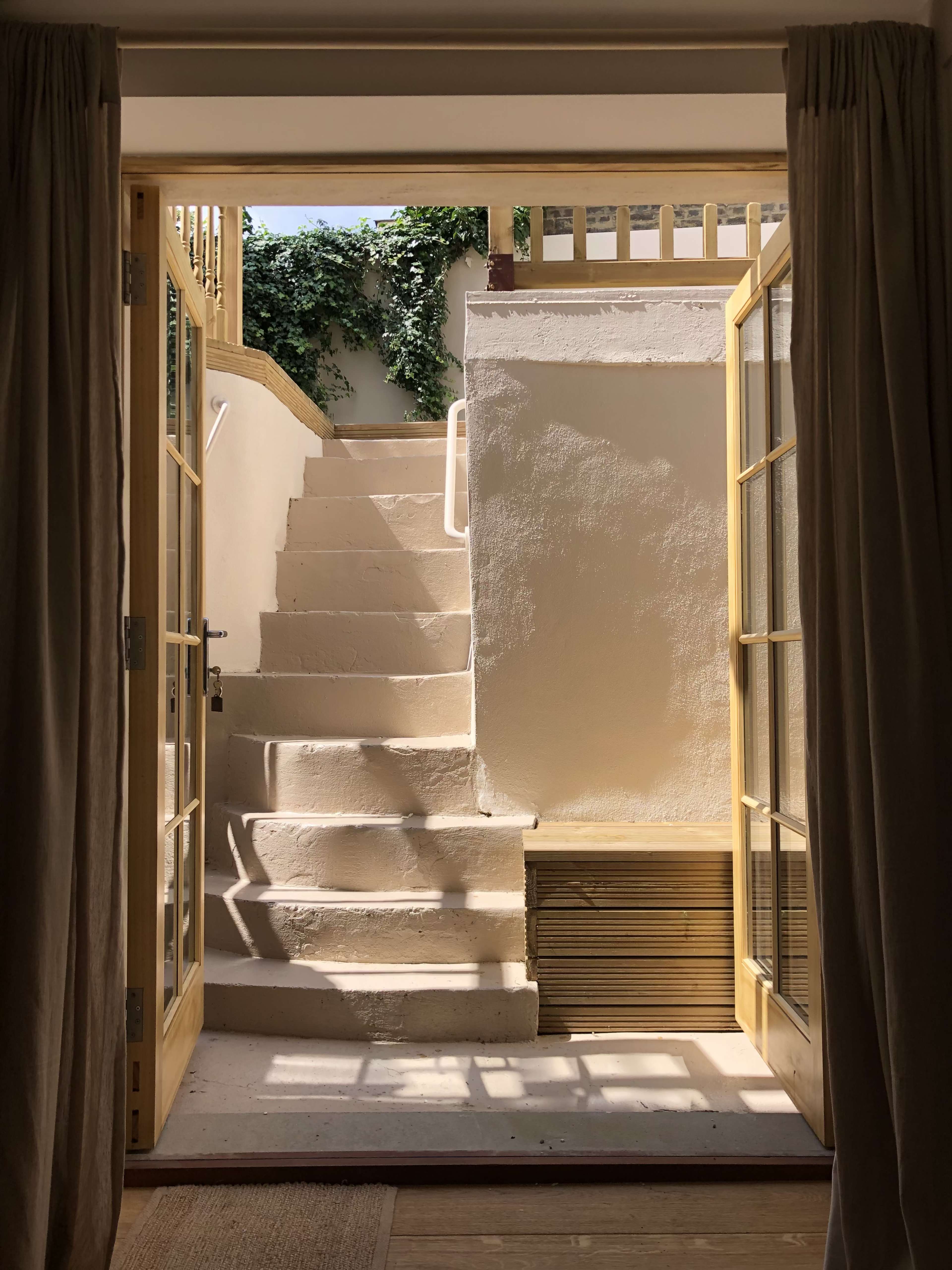 A staircase ascending from a room, framed by open double doors, with a wall covered in greenery visible at the top.