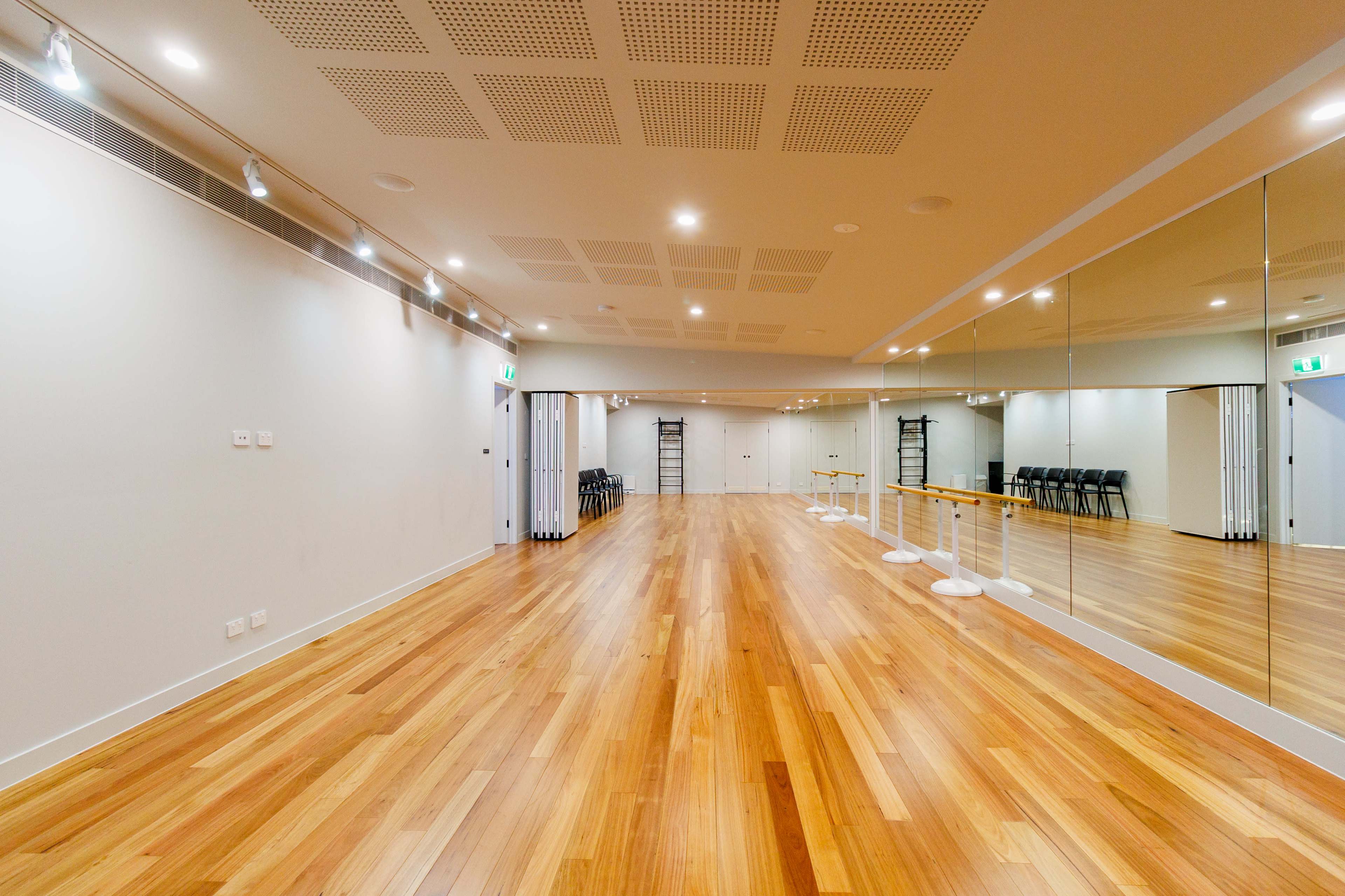 The image shows a spacious, well-lit dance studio with wooden flooring and large mirrors lining one wall.
