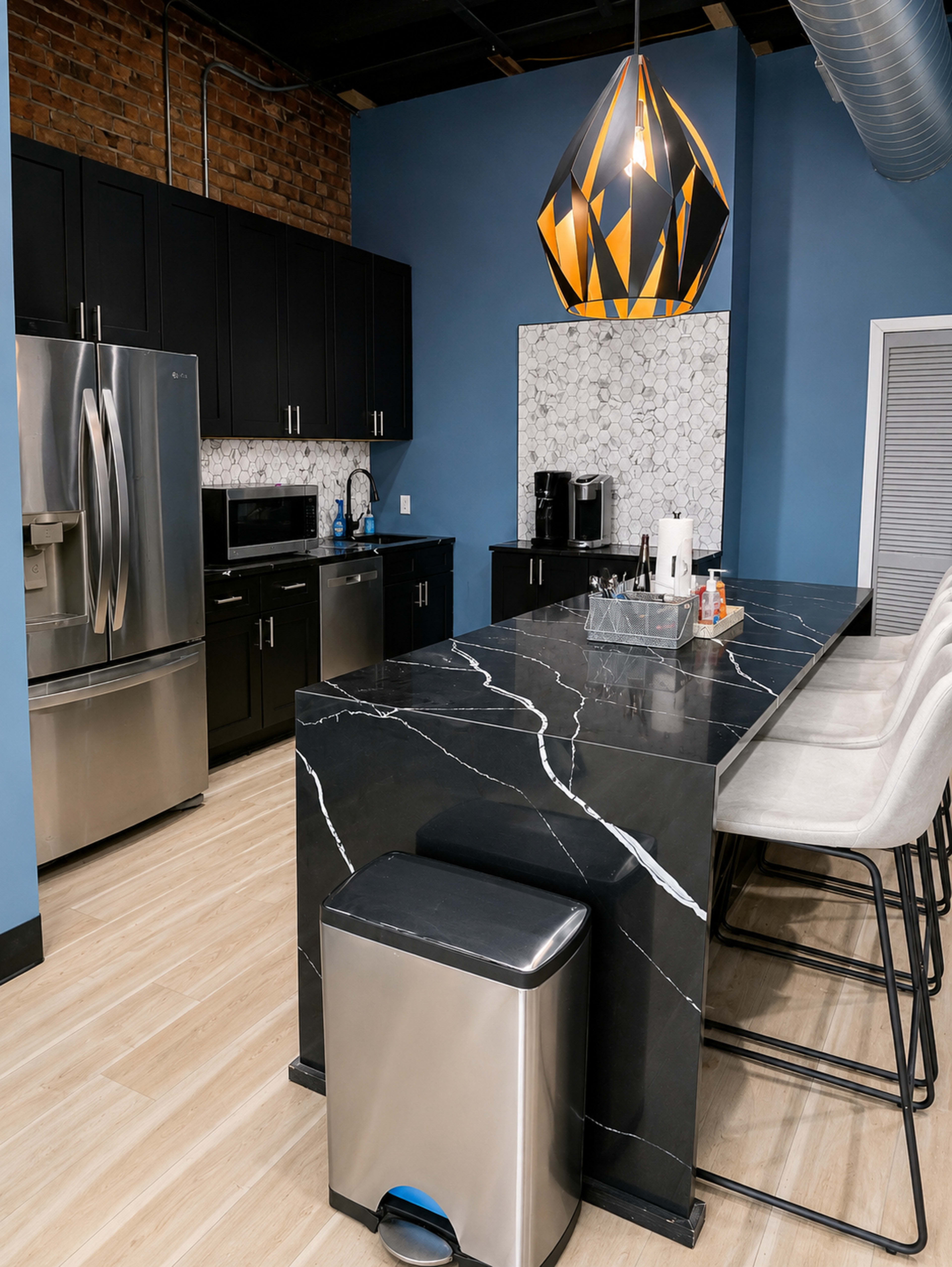 The image shows a modern kitchen featuring black cabinets, a large marble island with a sleek design, and a striking pendant light overhead.