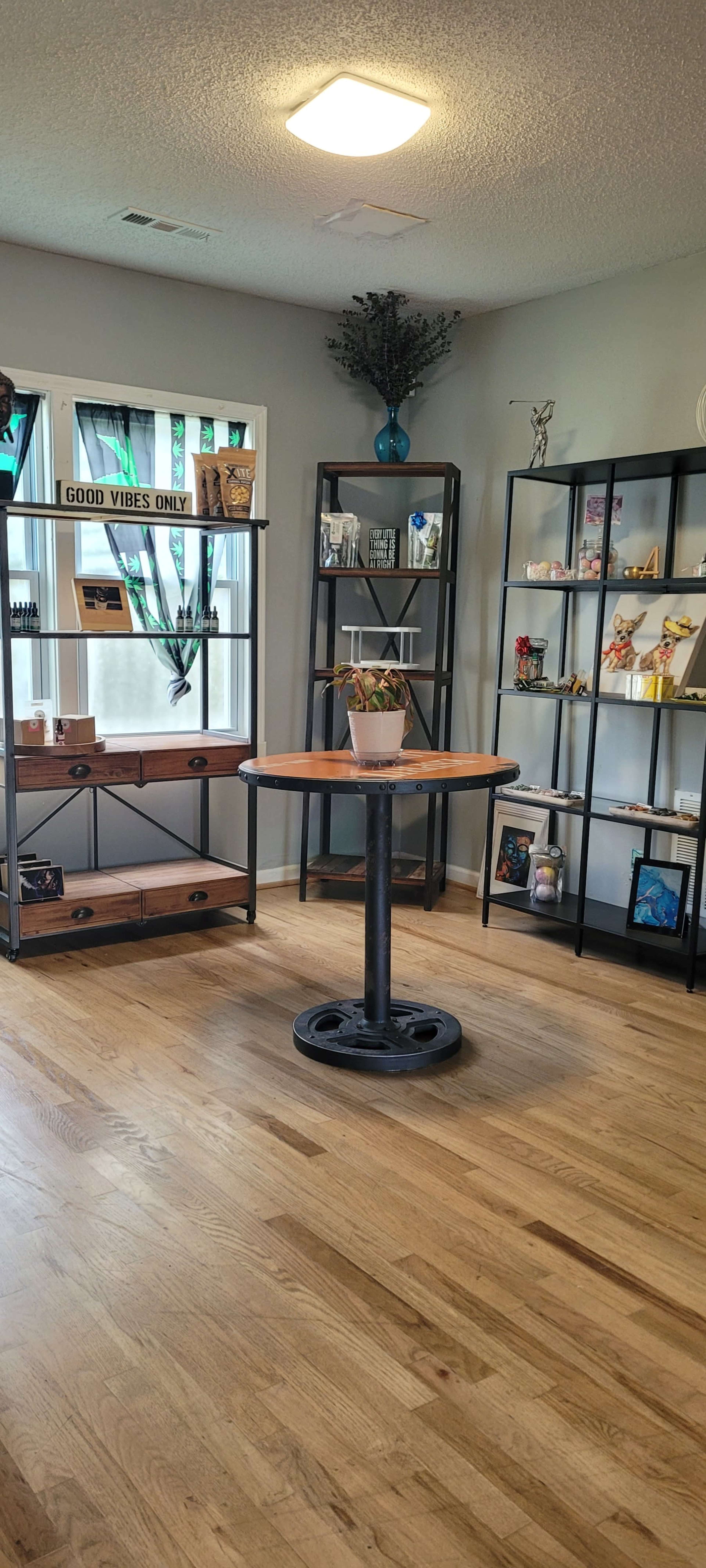 A room with wooden flooring, featuring shelves filled with decor and a round table in the center topped with a potted plant.