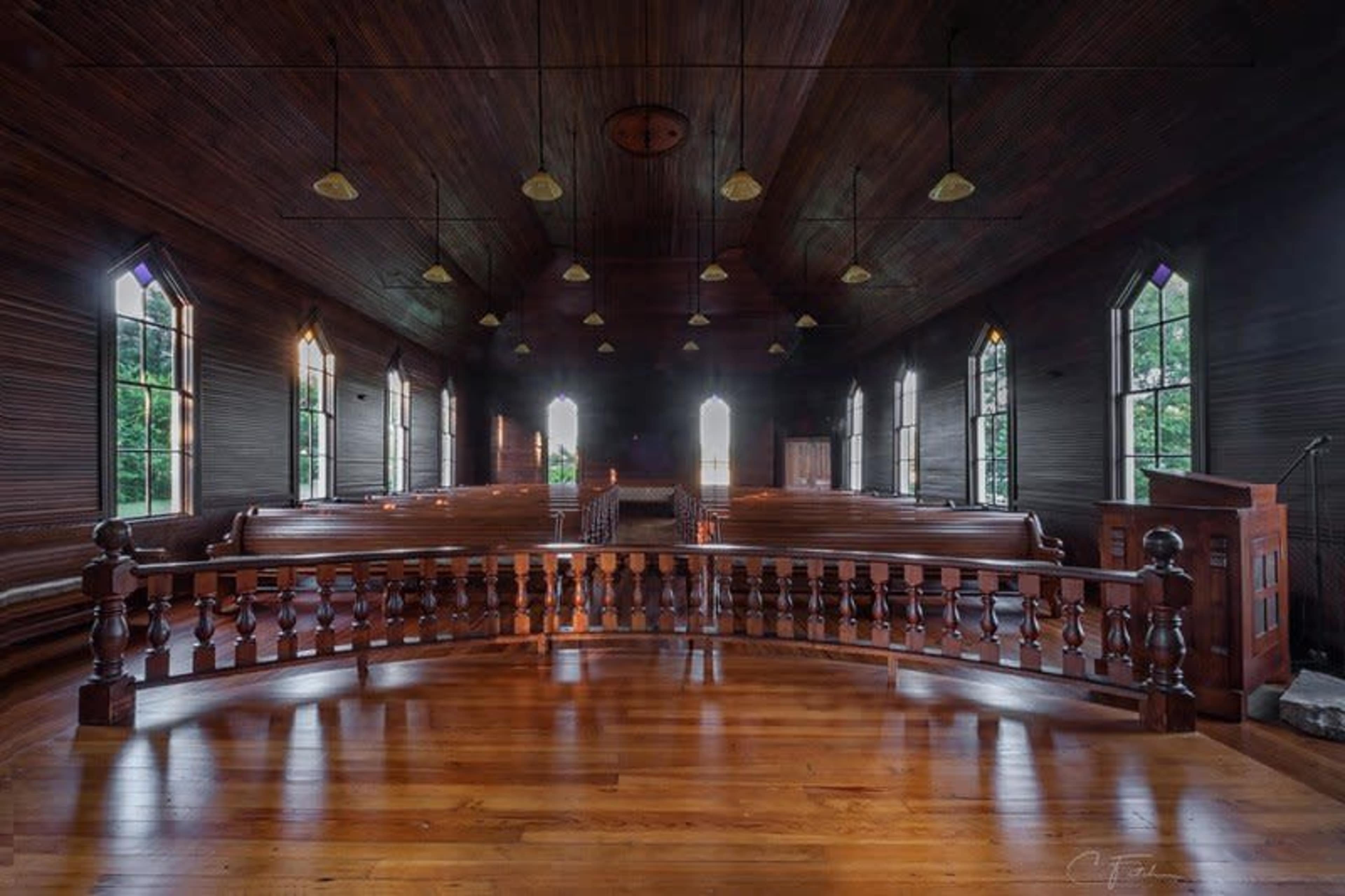 The image shows the interior of a church with wooden pews, large windows, and a decorative balcony surrounding the pulpit.