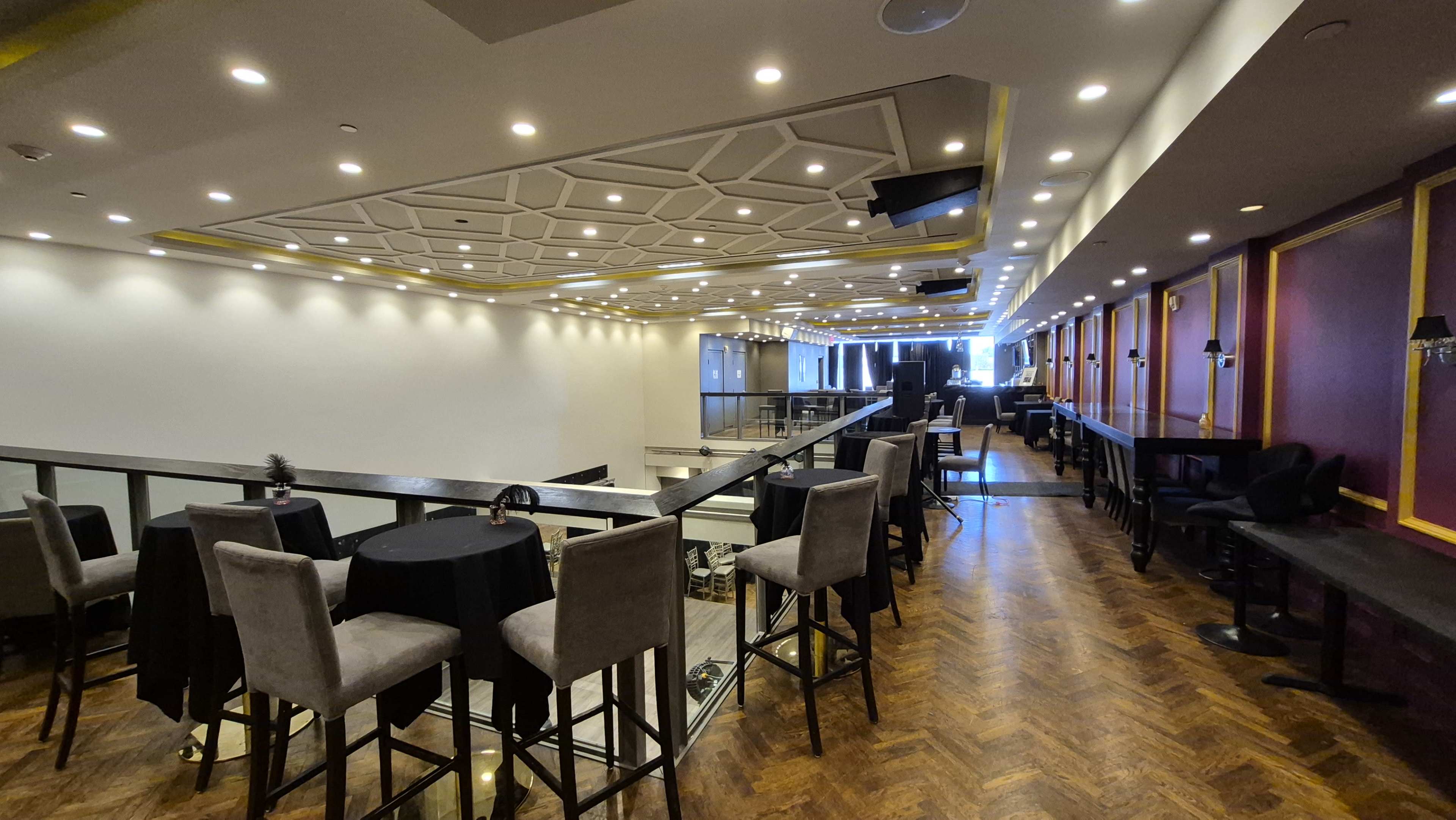 The image shows an interior view of a modern event space with high ceilings, multi-level seating, and soft lighting.