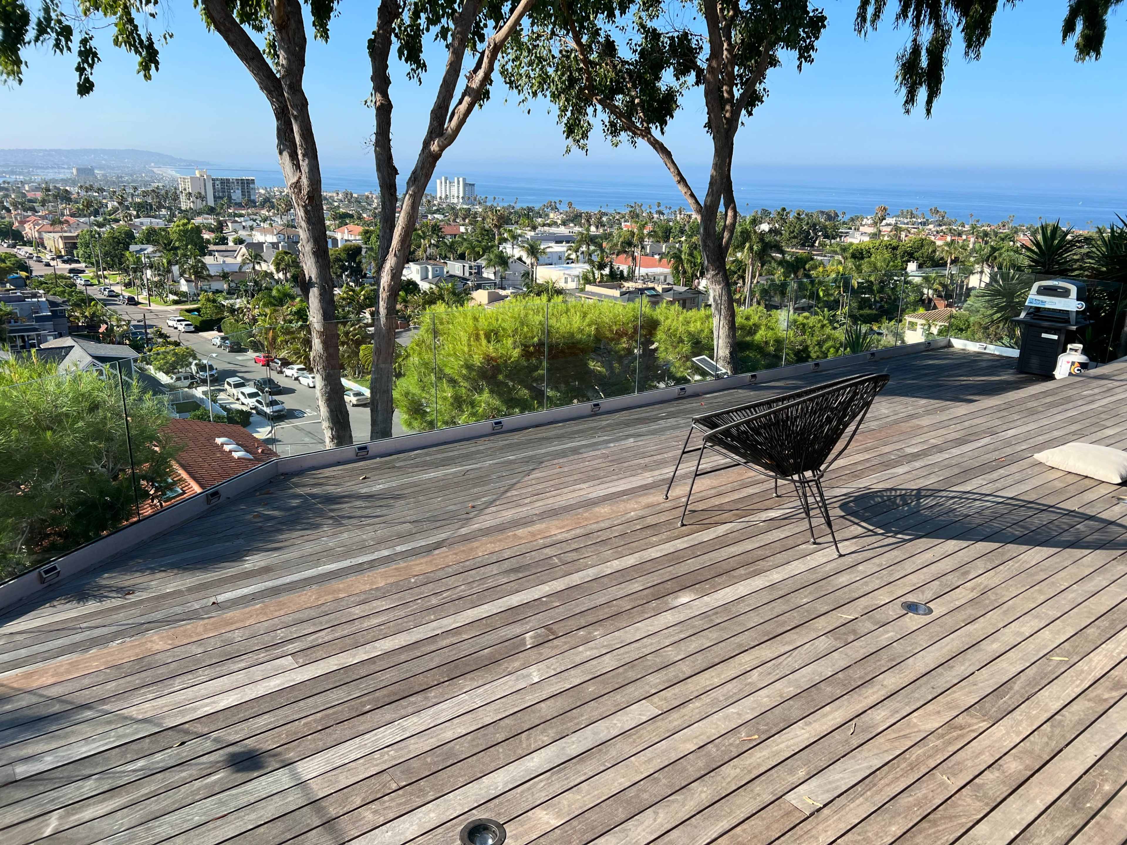 A wooden deck with a black chair overlooks a coastal view of a cityscape and the ocean in the distance.