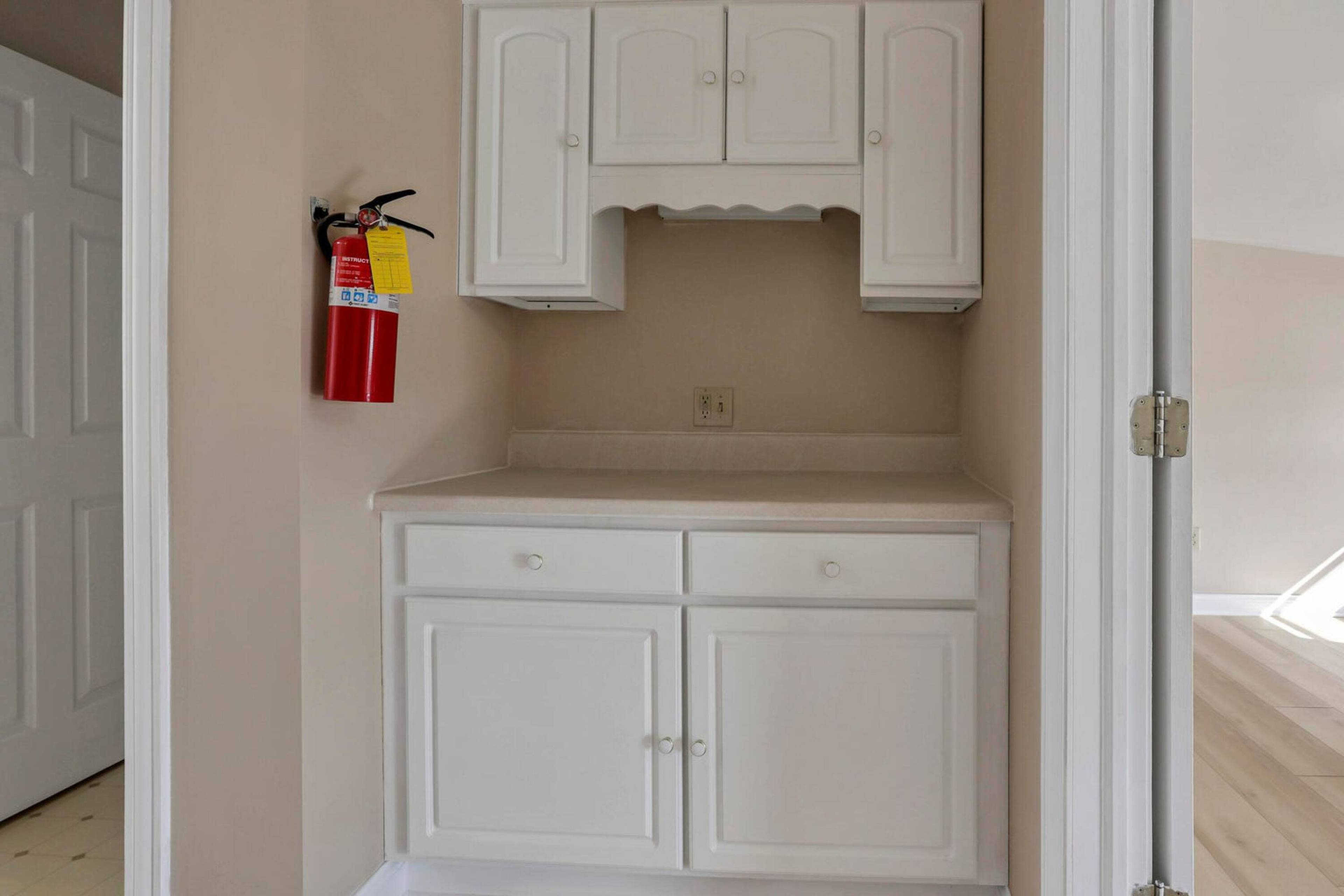 A small kitchen area with white cabinetry and a fire extinguisher mounted on the wall.