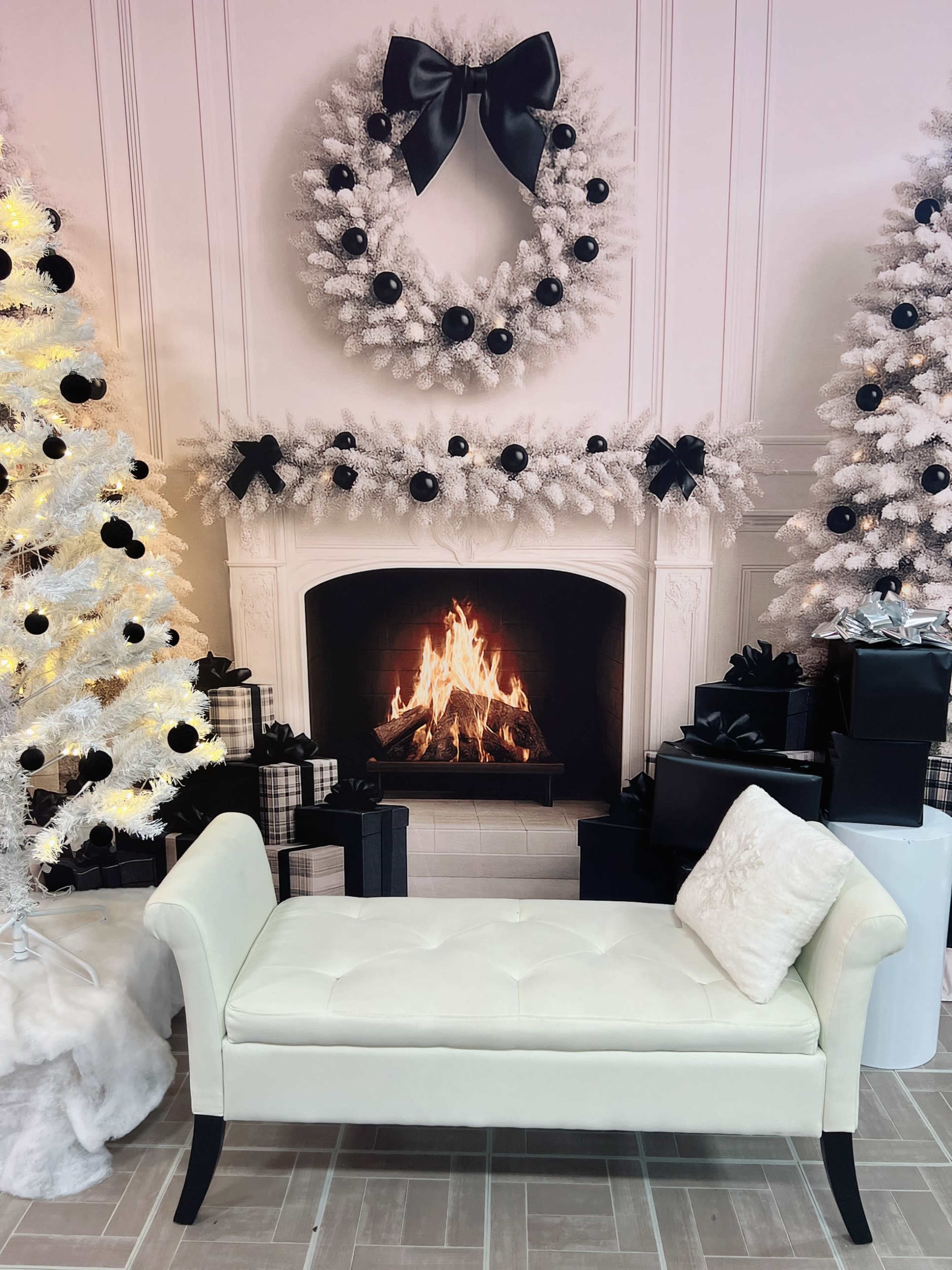 A white upholstered bench is positioned in front of a lit fireplace, surrounded by decorated Christmas trees and wreaths.
