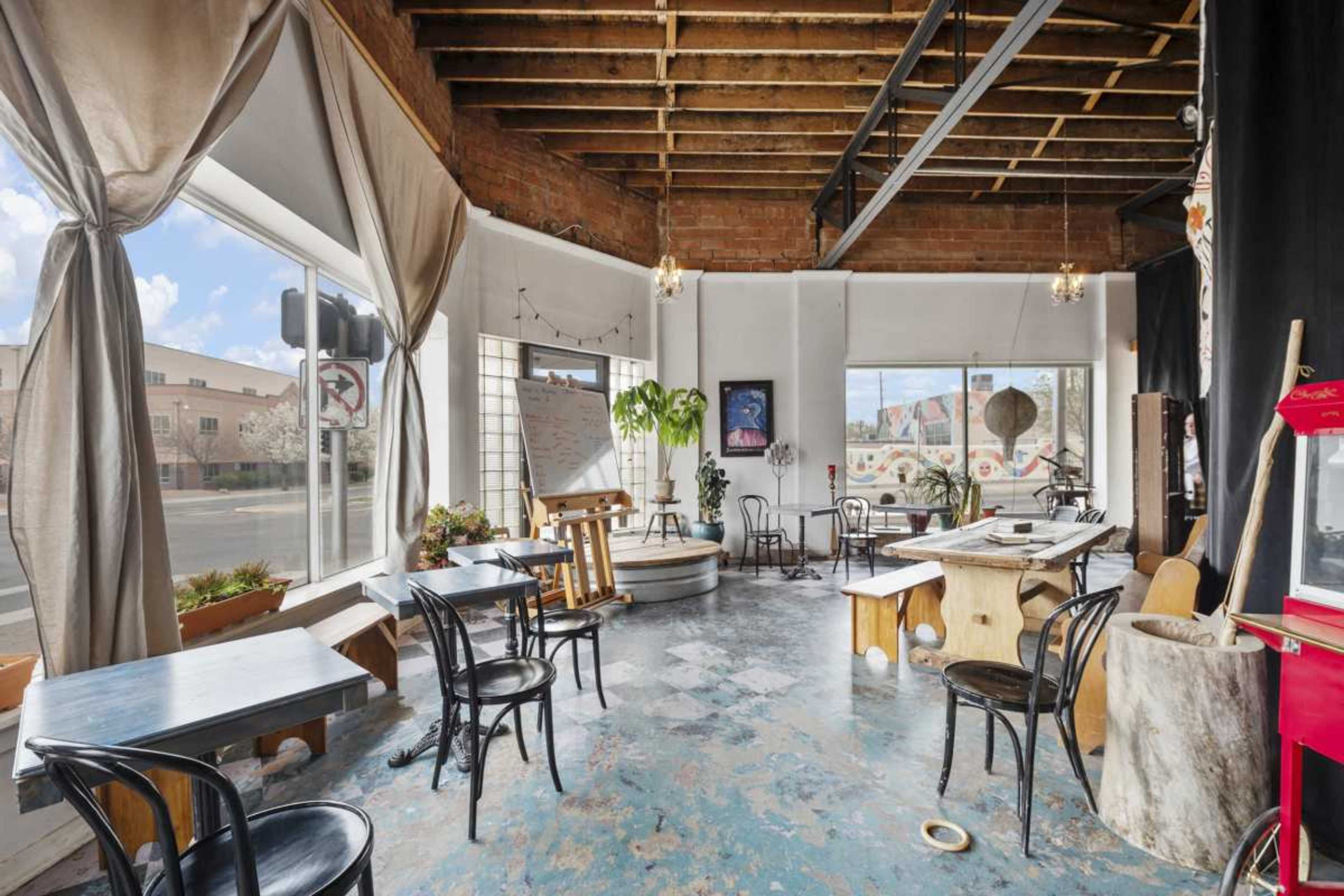 A spacious, industrial-style cafe with large windows, wooden beams, and scattered tables and chairs.