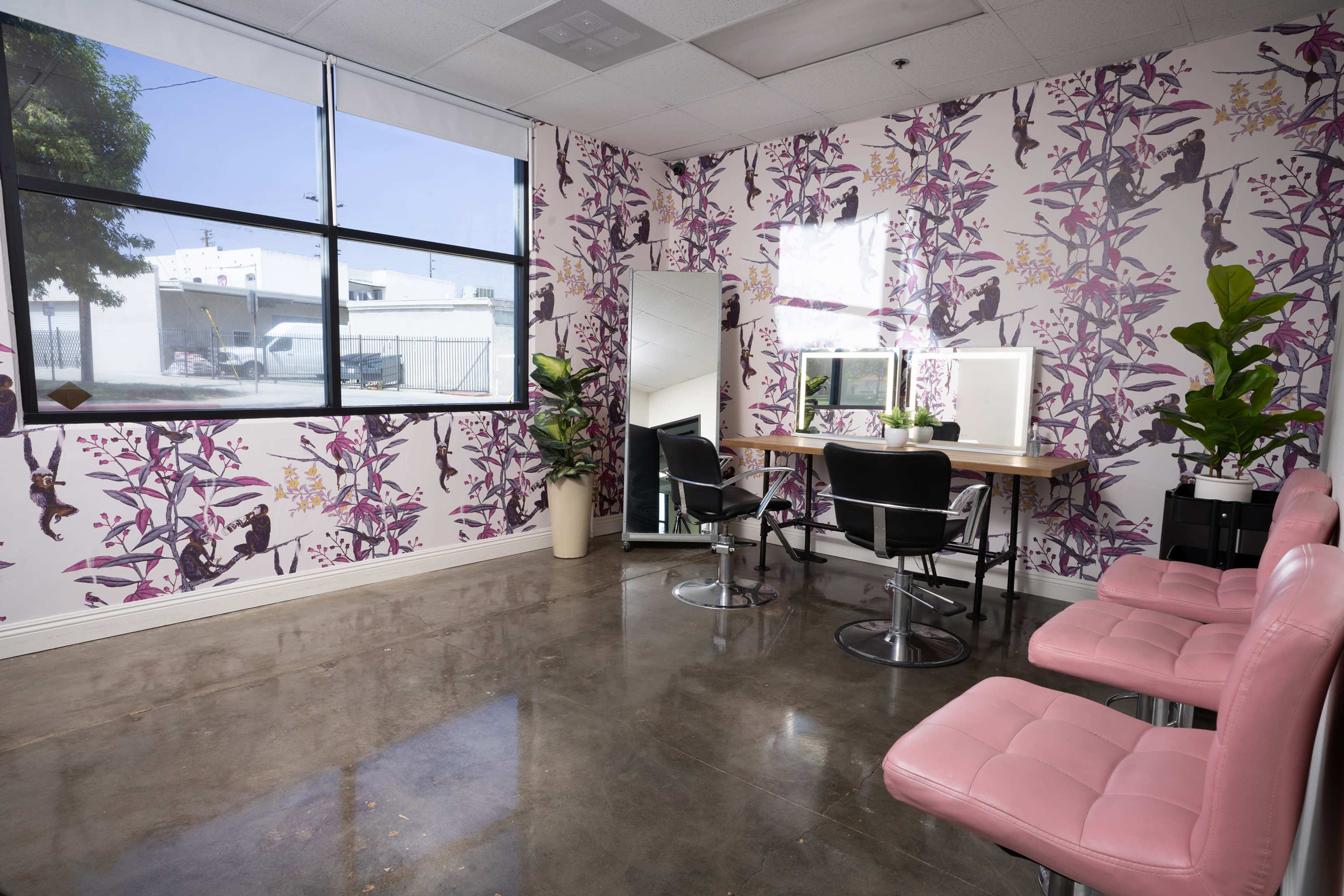 The image shows a modern room with pink chairs, a wooden table, and large windows, surrounded by floral-patterned wallpaper.